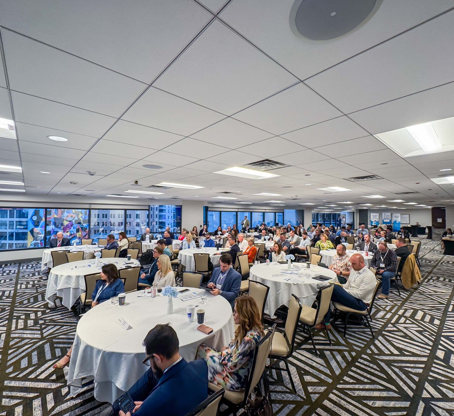 Conference room setup with round tables and geometric carpet pattern during a professional gathering.