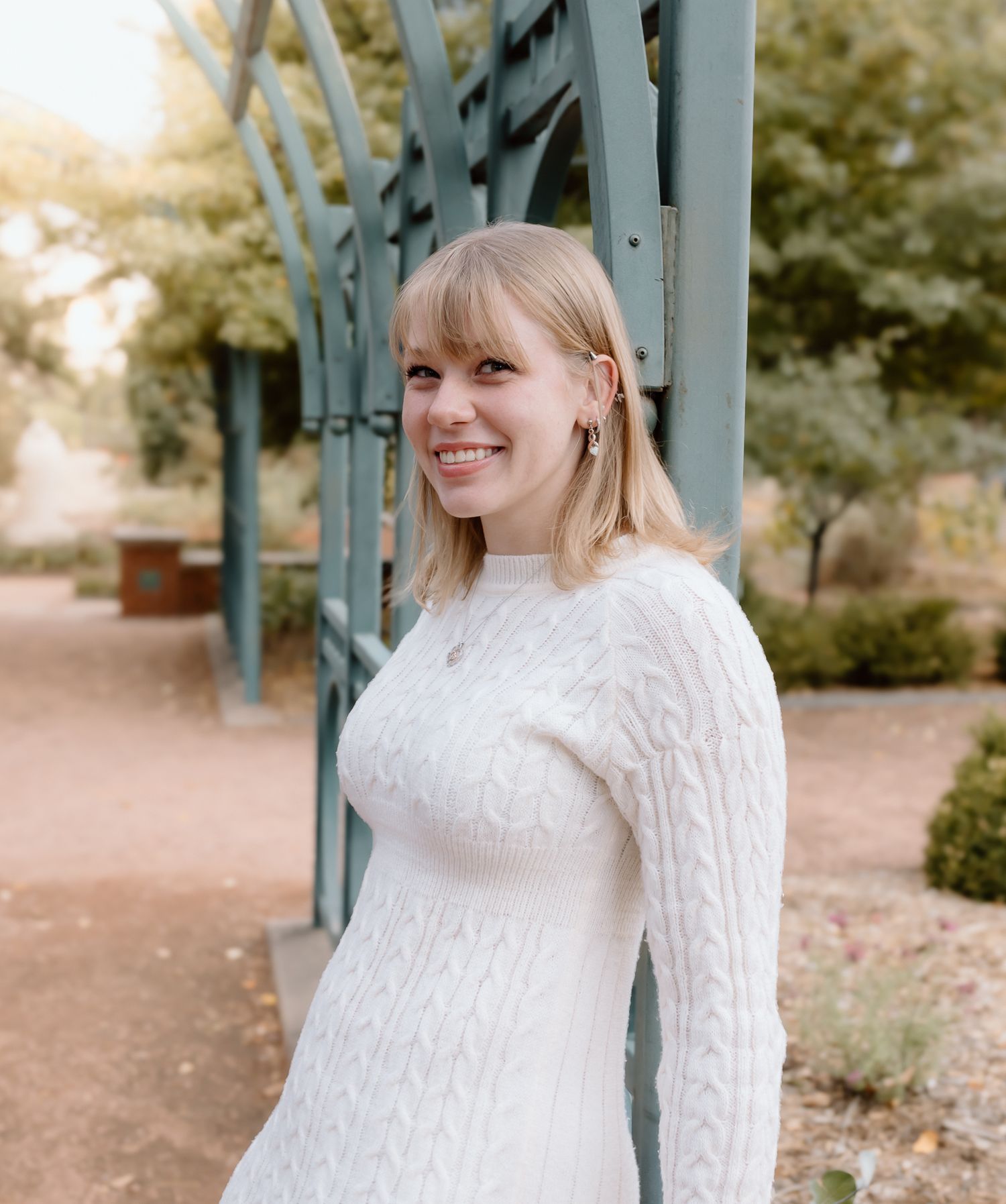 Person in white cable knit sweater poses against blue structural beam in outdoor setting during autumn.
