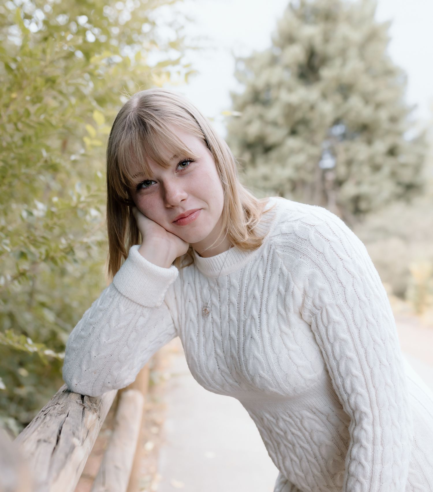 A person wearing a cozy white cable knit sweater poses outdoors against a soft autumn background.