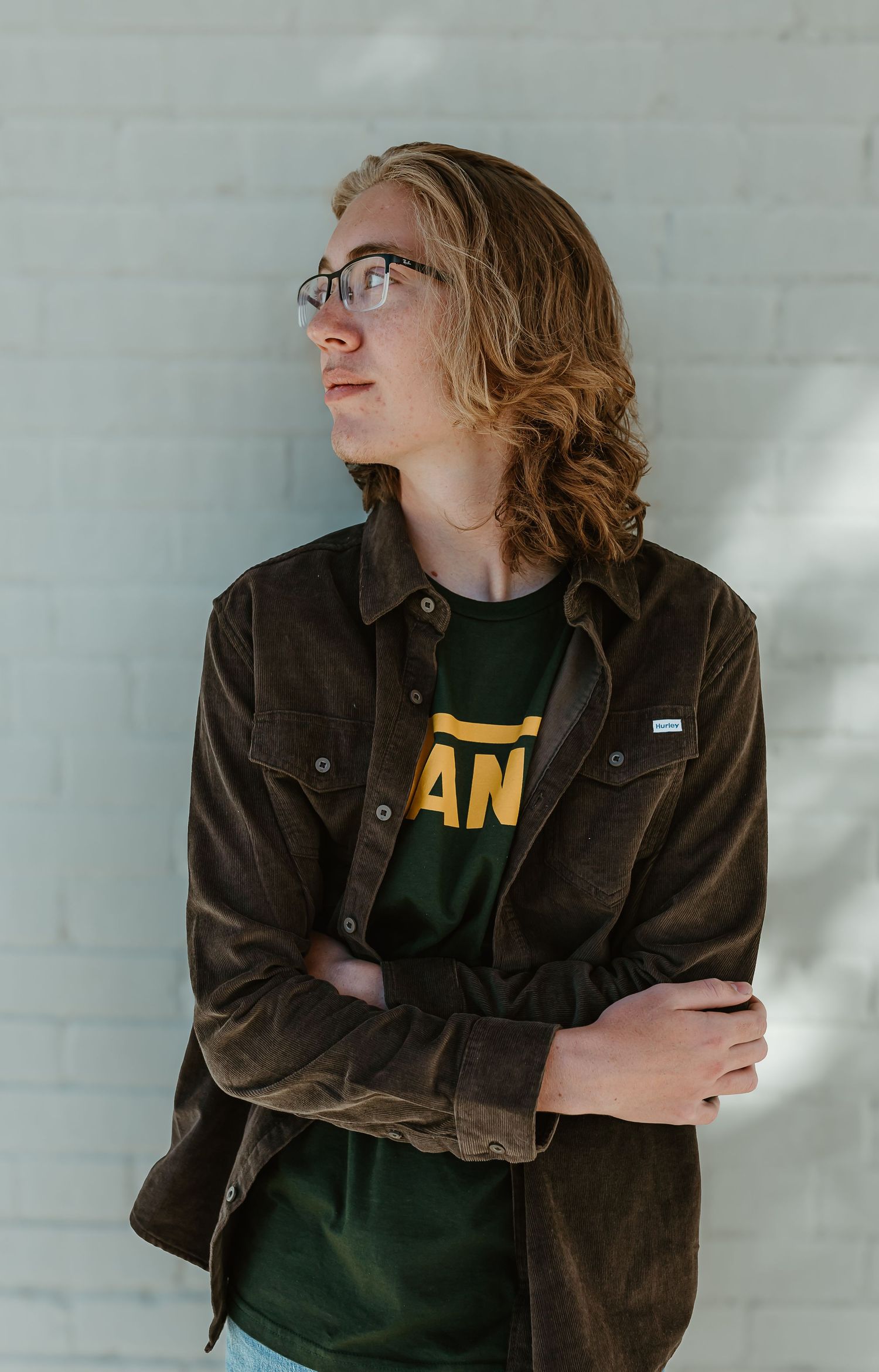 Person in brown jacket and dark shirt poses against white wall in artistic portrait series.