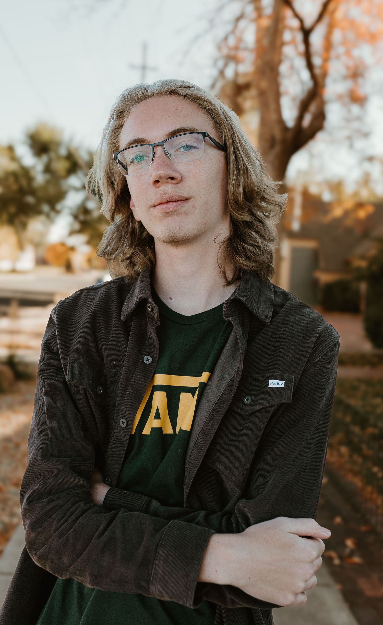 Person in glasses and dark jacket leans against wall during golden autumn sunset.