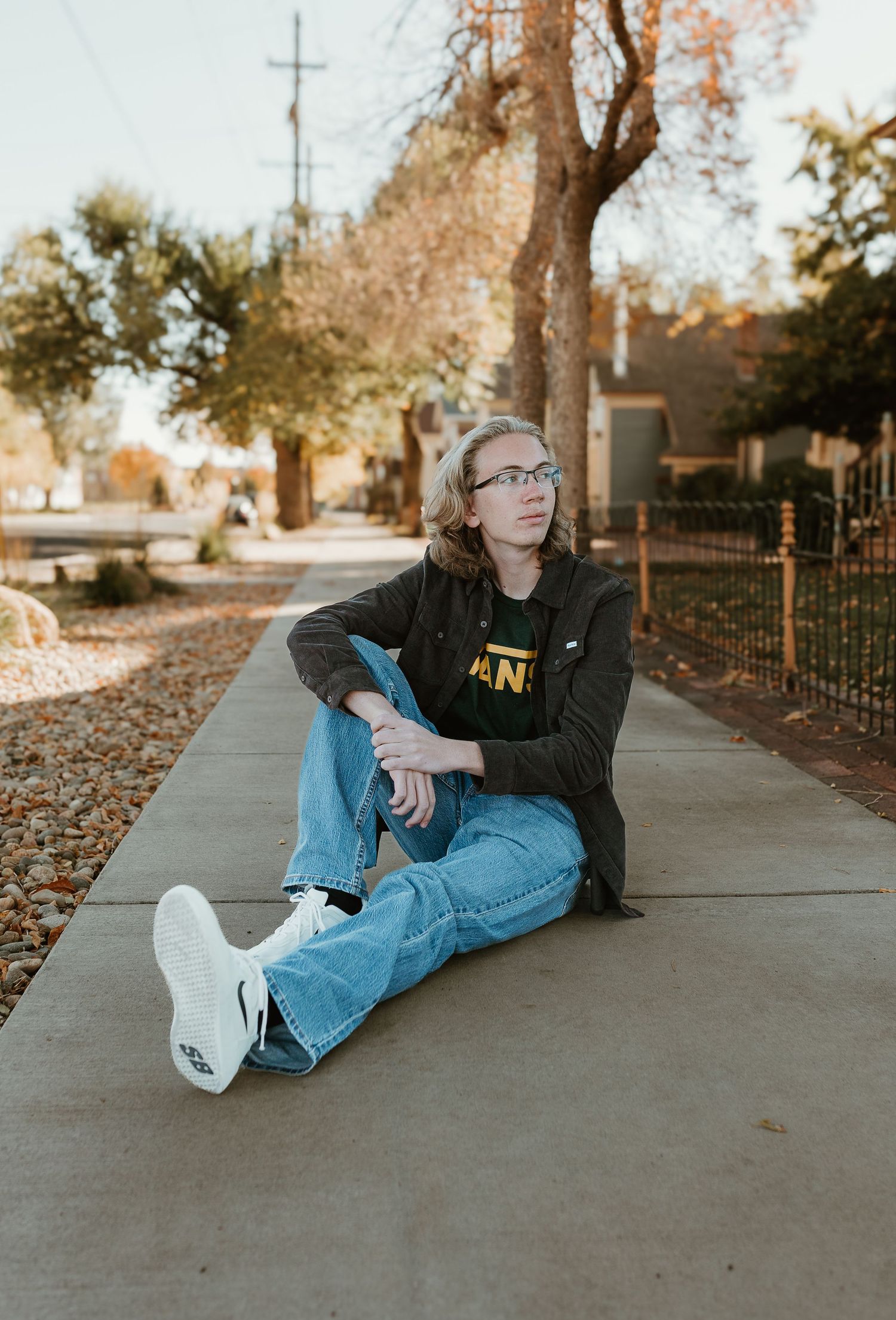 Person in dark clothing and jeans relaxes on a sidewalk surrounded by fall leaves.
