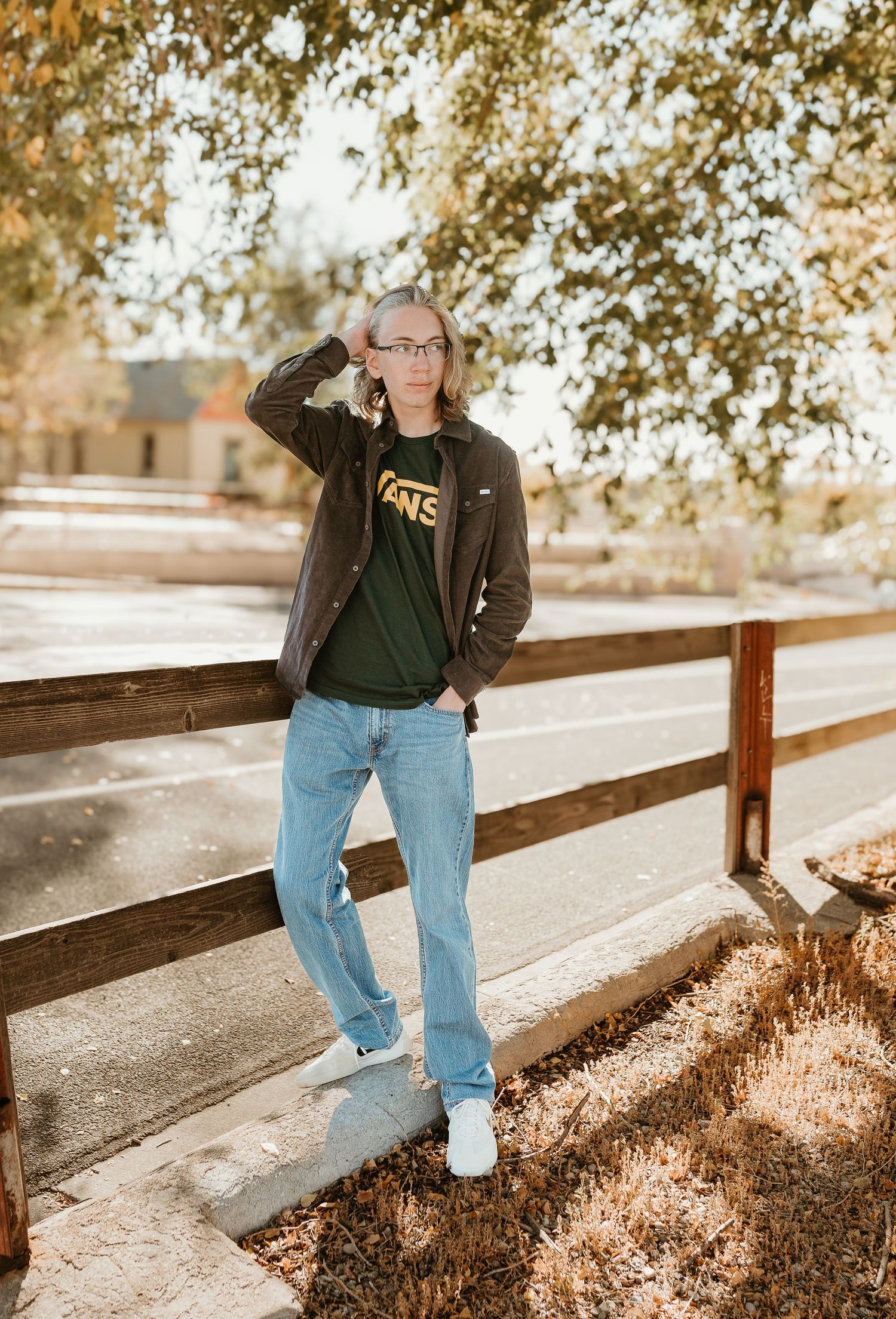 Autumn scene showing someone sitting on a wooden fence with sunlit trees in the background.