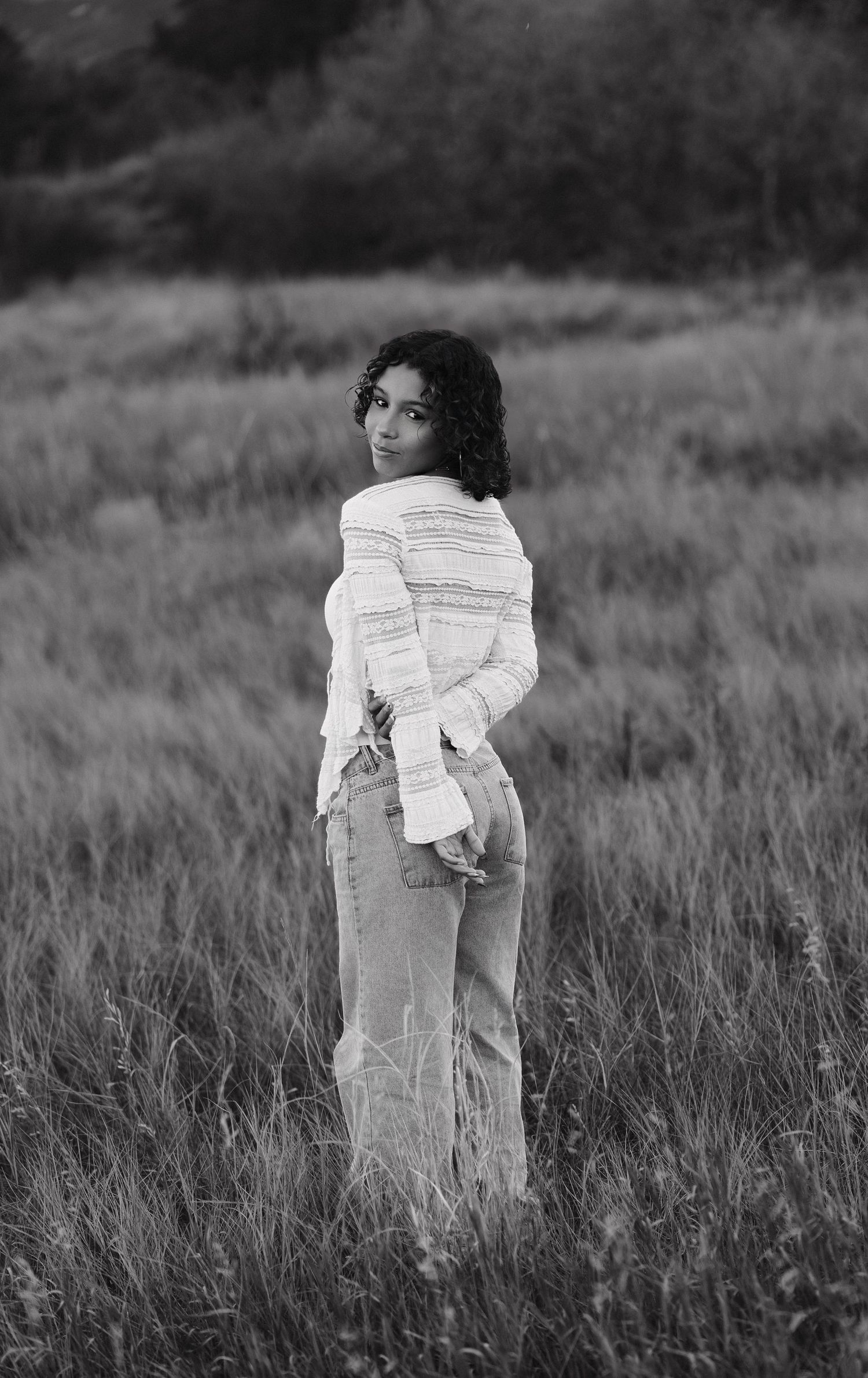 A black and white portrait of someone in casual attire standing in a serene meadow landscape.