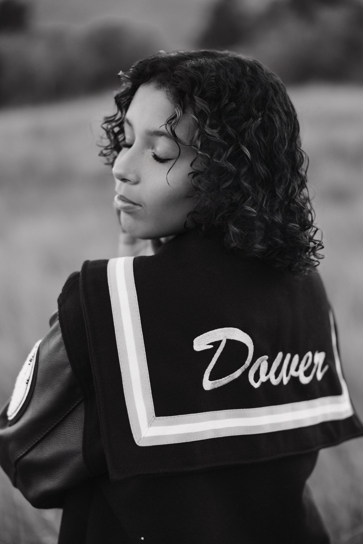 Black and white portrait of person with curly hair wearing a jacket with 'Dover' text on sailor-style collar.