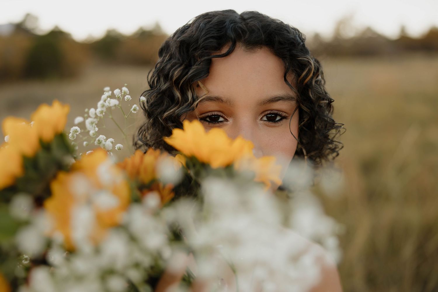 A person stands in a field of yellow and white wildflowers during golden hour with soft bokeh lighting.