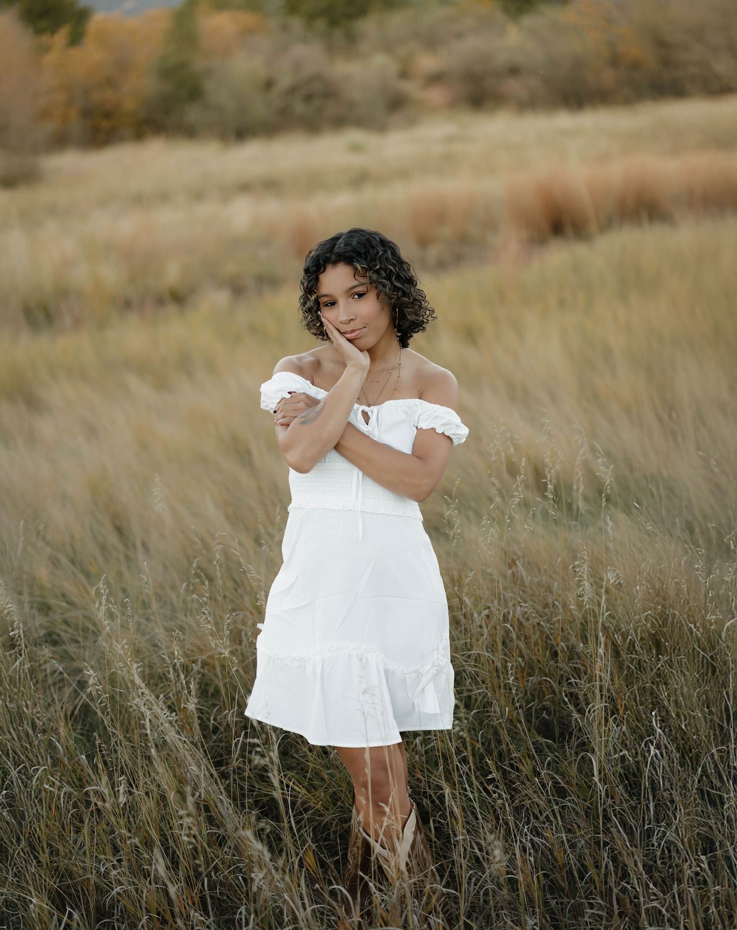 A dreamy portrait of someone wearing a white off-shoulder dress while standing in a sun-kissed field of tall grass.