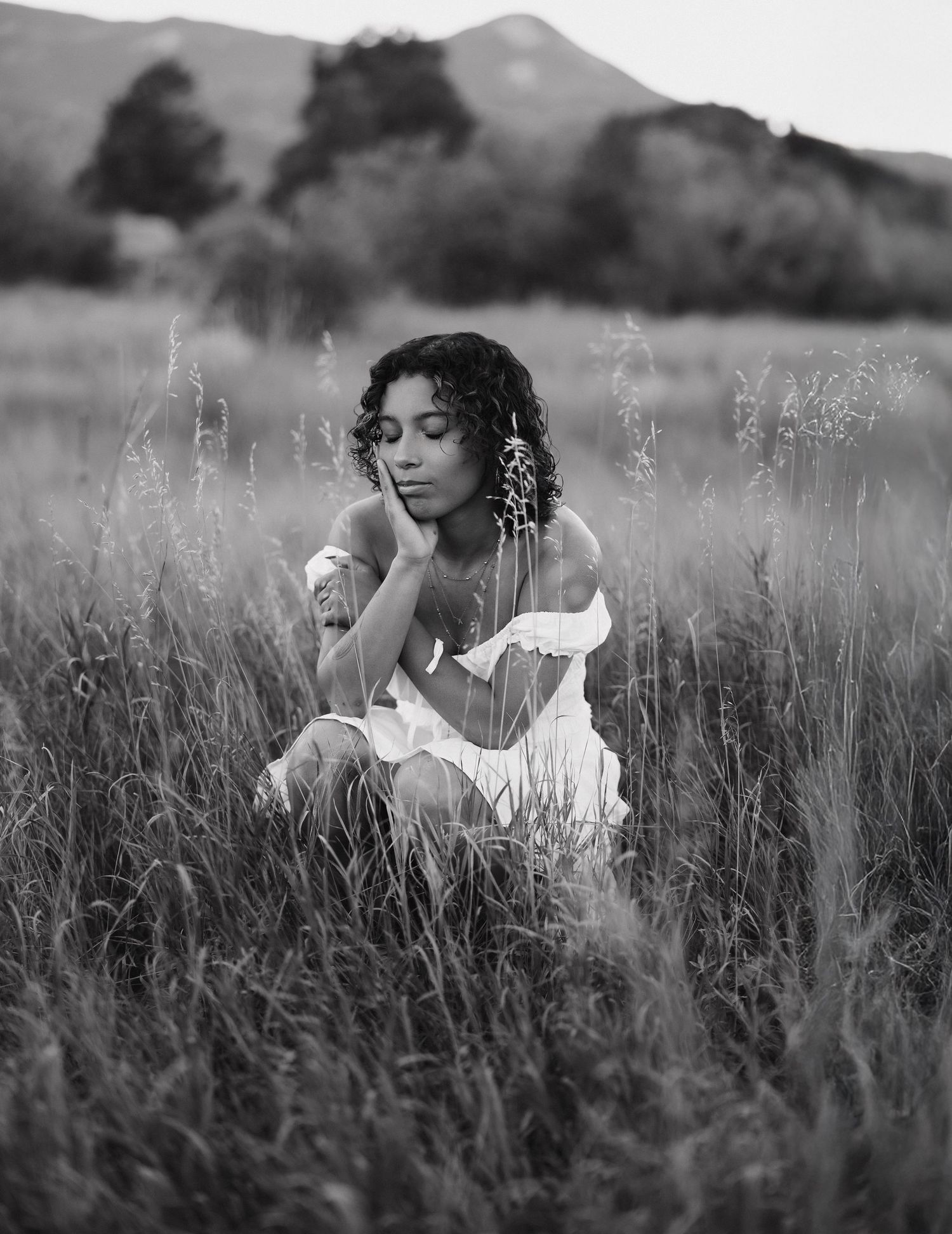 Artistic black and white portraits of someone wearing a white dress amid wild grasses in a meadow.