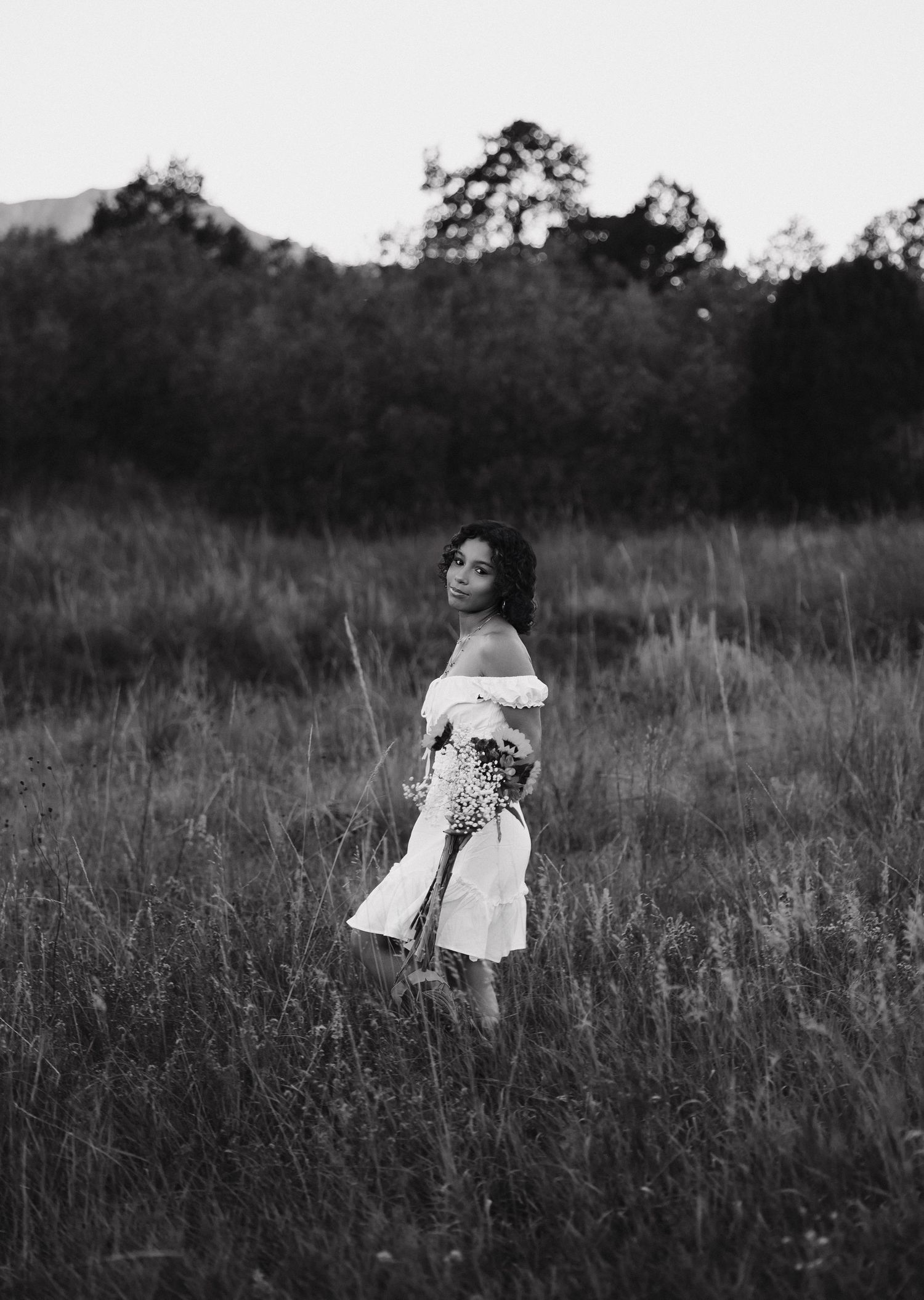 A series of black and white photographs showing a person in a white dress sitting in a tall grass field.