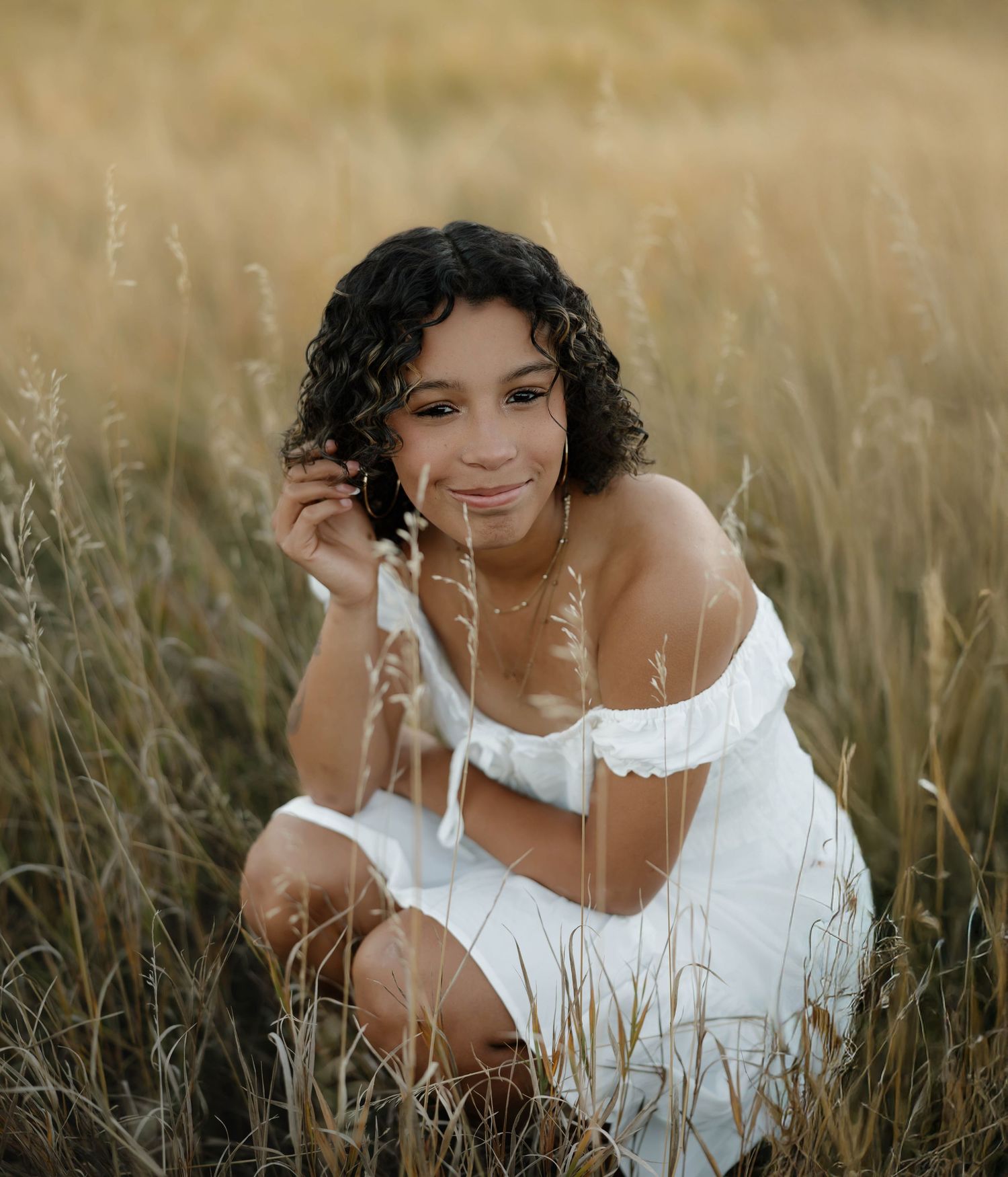 Dreamy outdoor portraits in golden light showing someone in white dress laying in tall grass field.