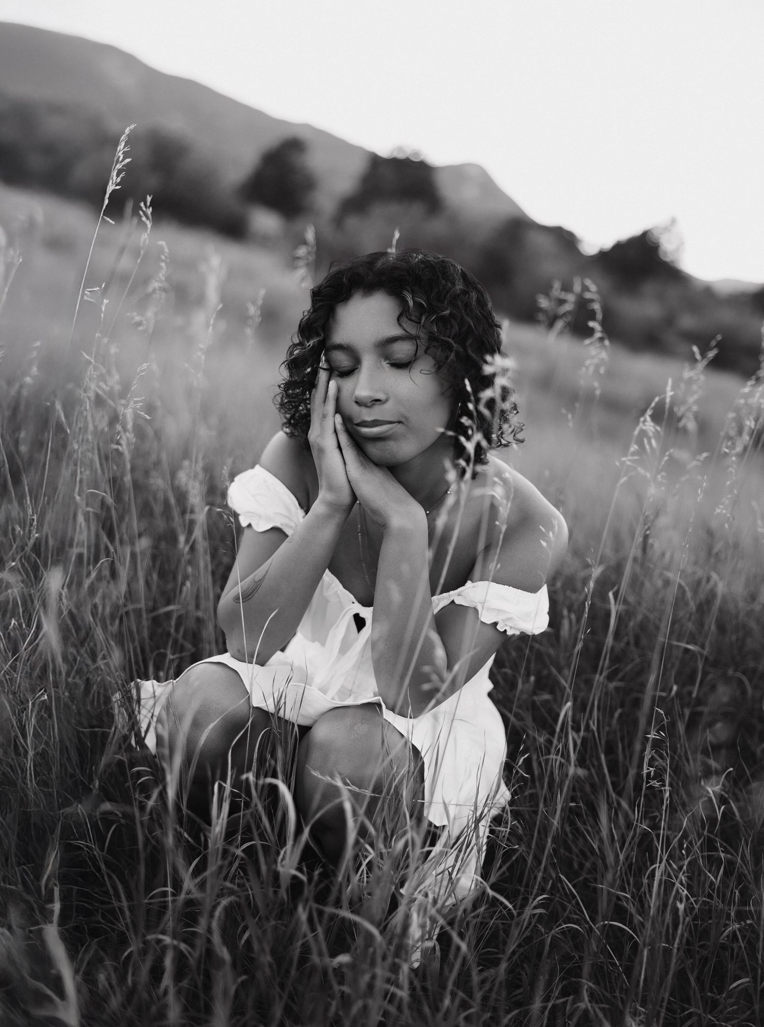 Black and white artistic photograph series showing a person sitting in a tall grass meadow in dreamy natural lighting.