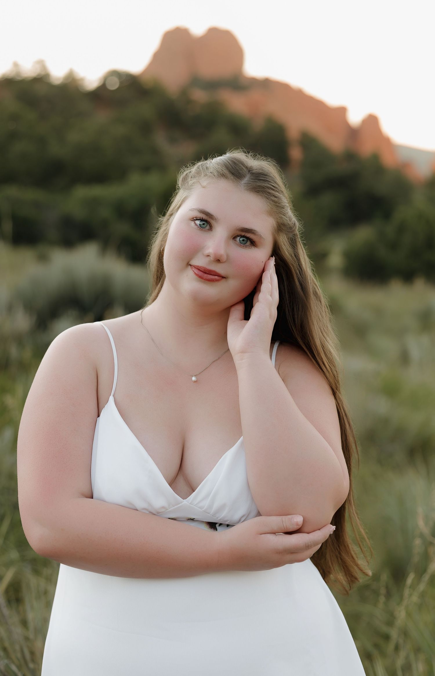 A person in a white dress poses outdoors at sunset with red rock formations visible in the background.