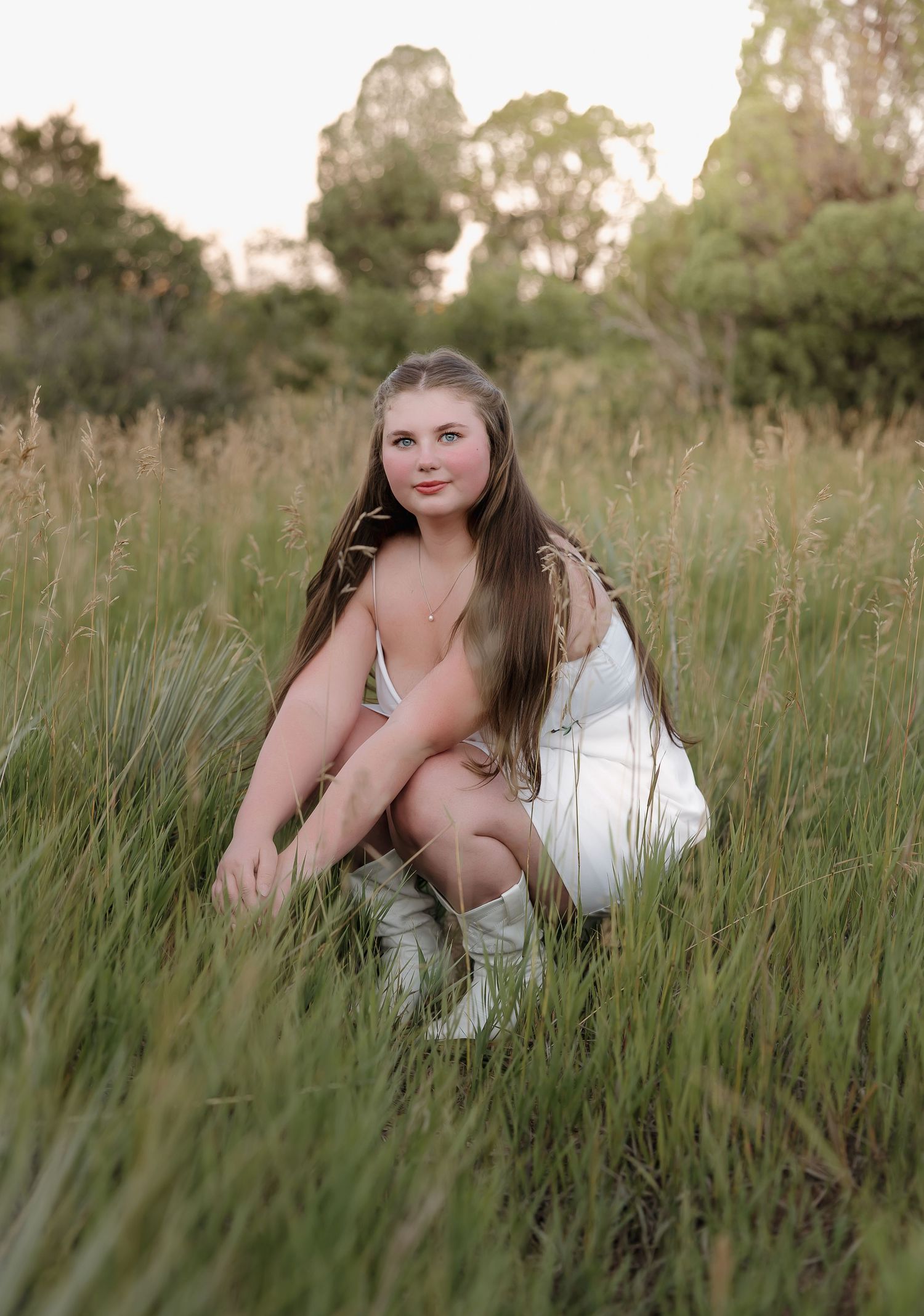 A figure in a white dress reclines in tall grass during a golden hour outdoor photo session.