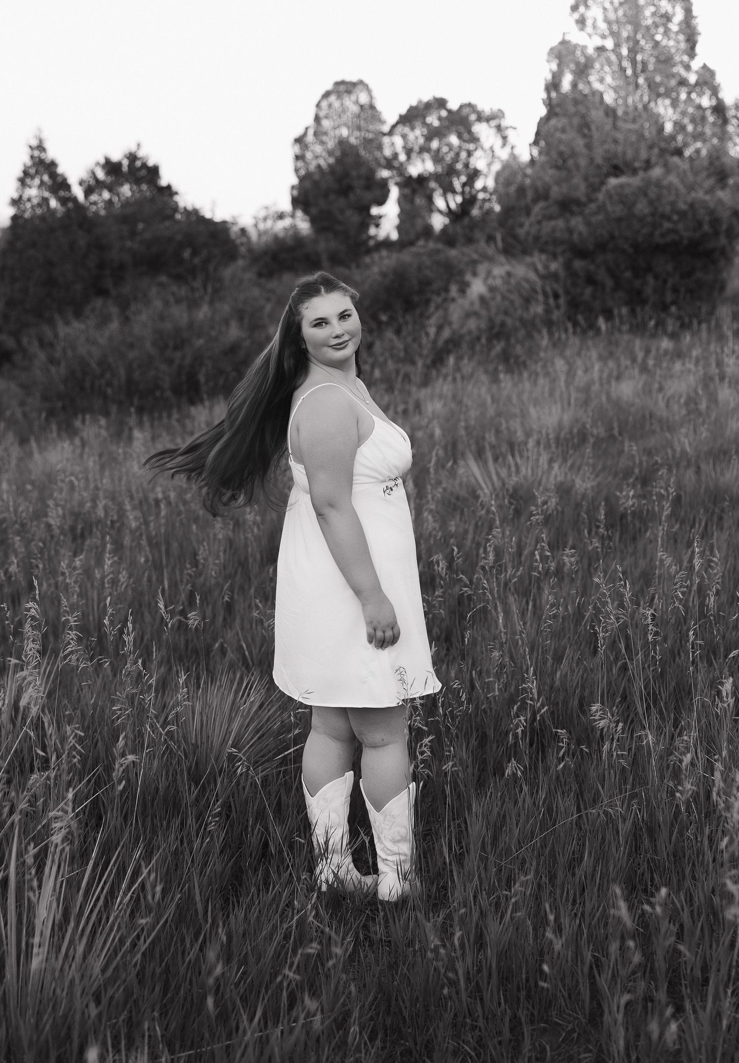 Black and white portrait captured in a tall grass field with trees in the background.