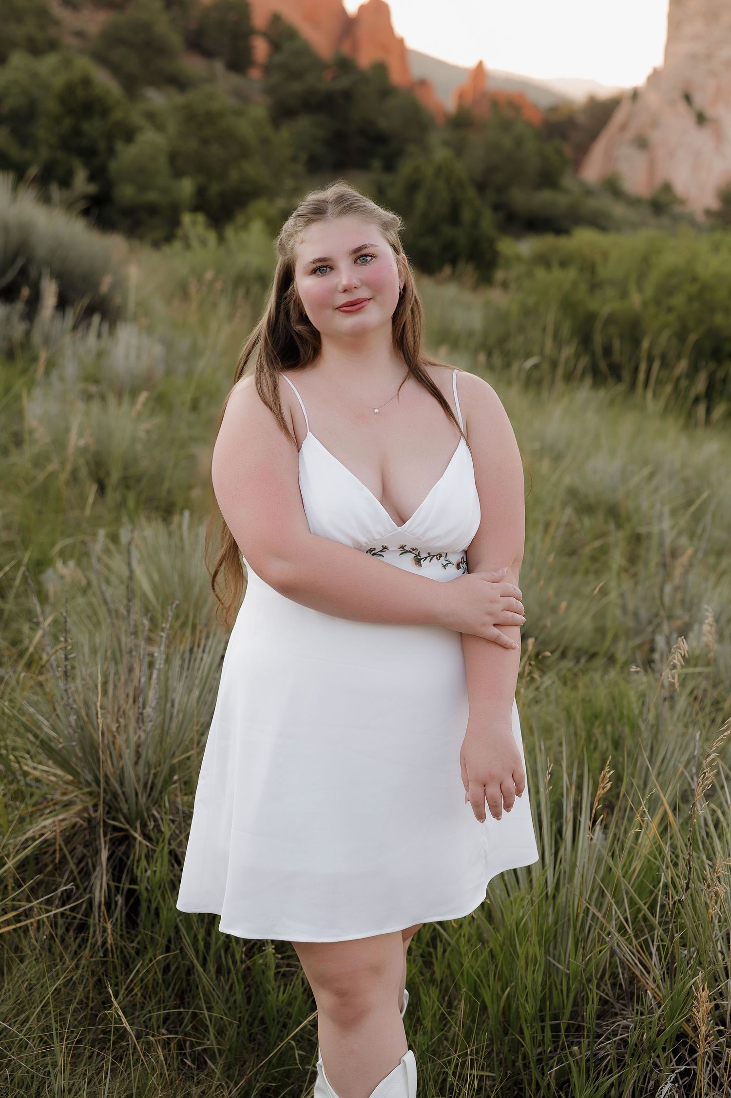 A white dress photoshoot in a scenic outdoor setting with red rock formations and natural greenery in the background.