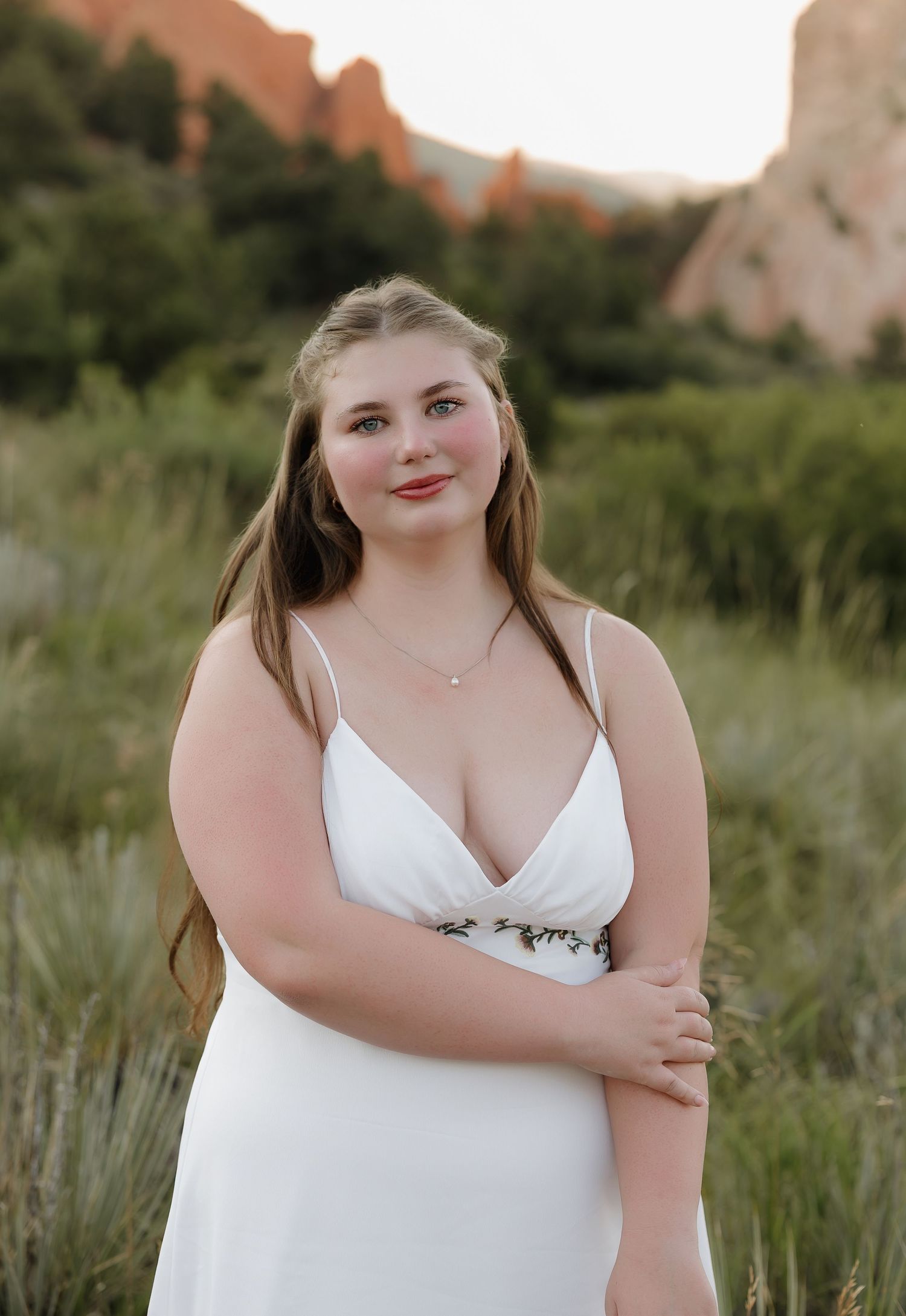 A white summer dress stands out against the natural backdrop of a grassy field and distant cliffs.