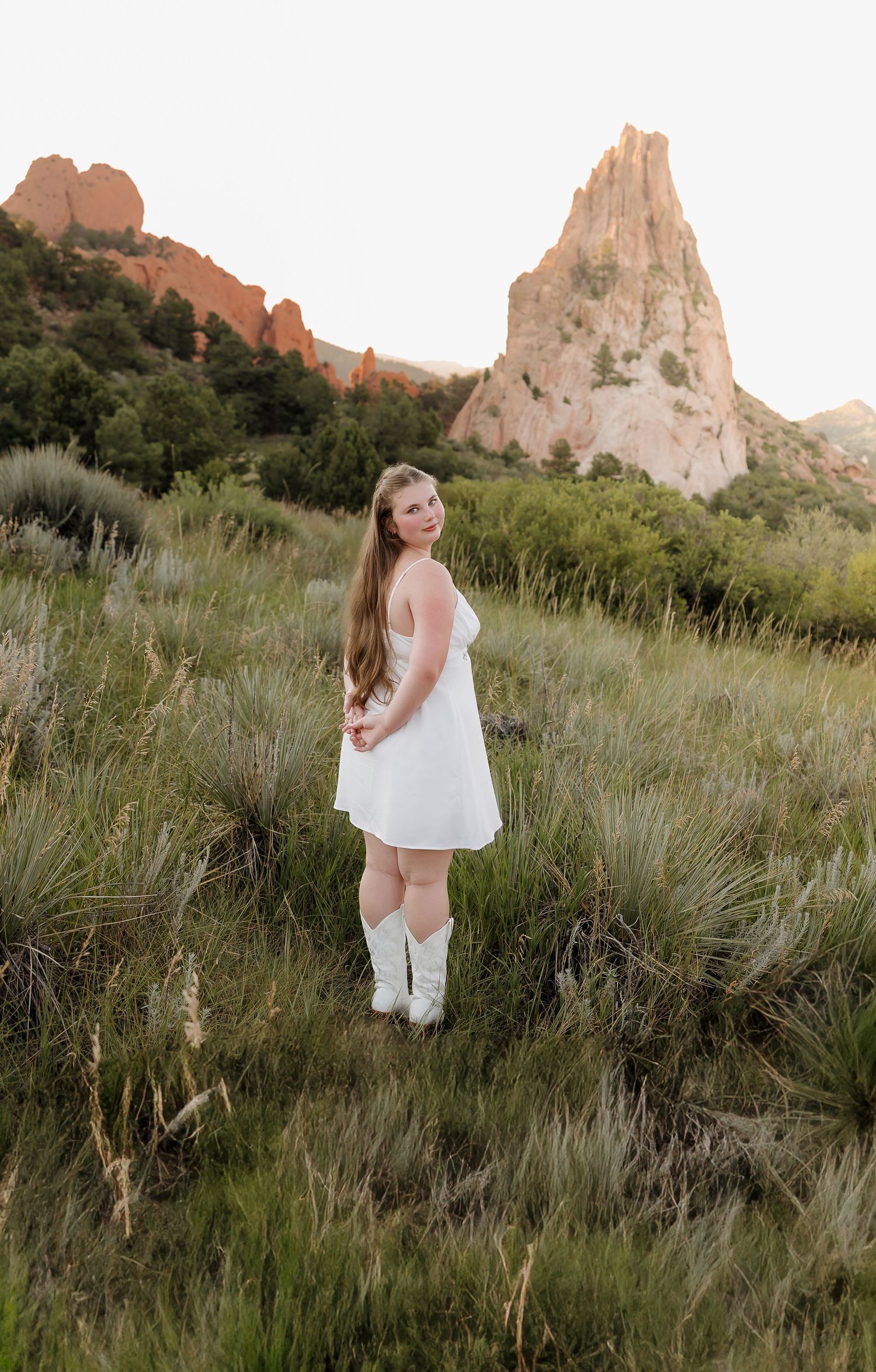 Woman in white dress poses in front of red rock formations at Garden of the Gods during sunset.