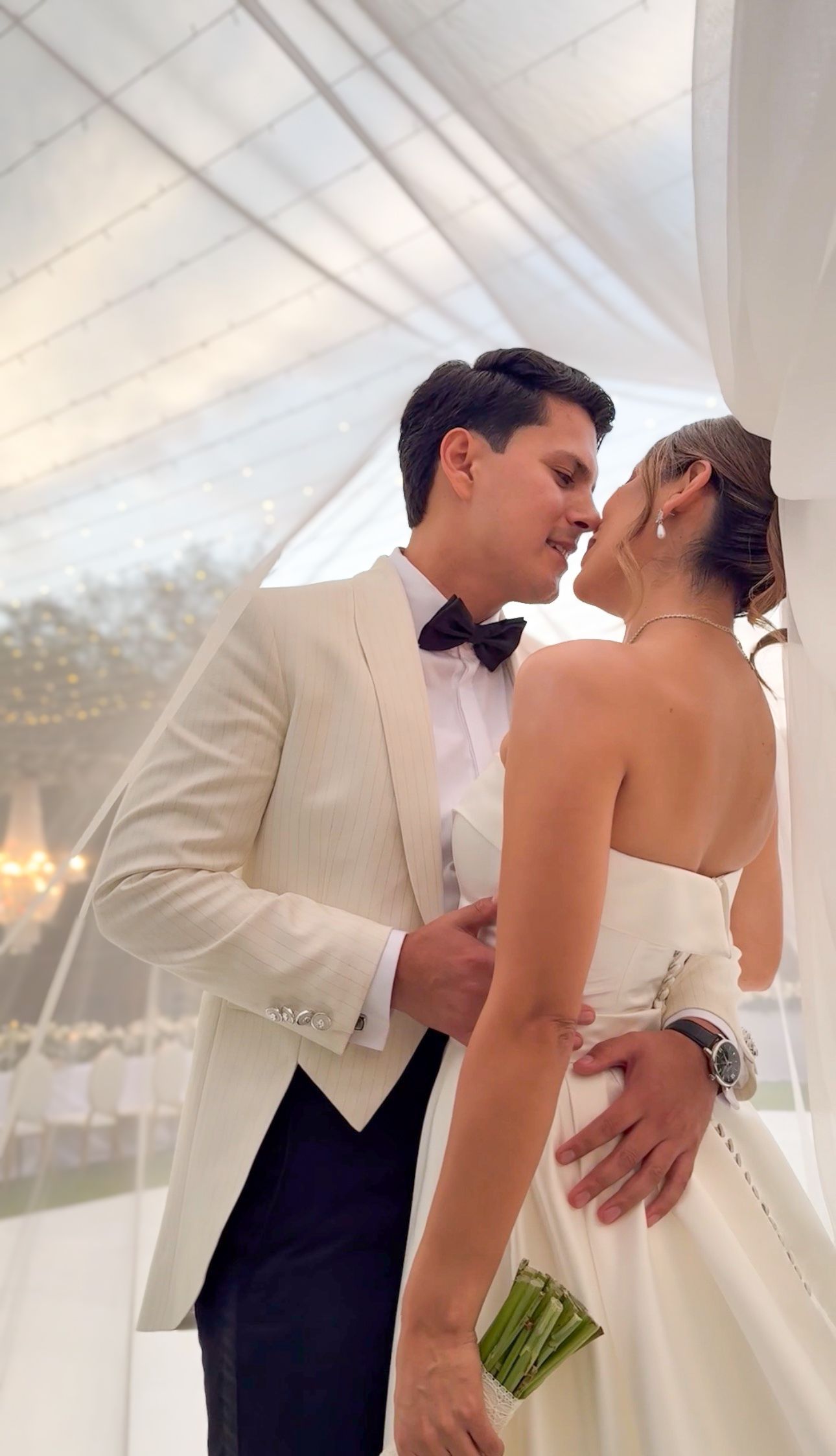 Person in red dress pinning boutonniere on someone wearing white formal attire outdoors.