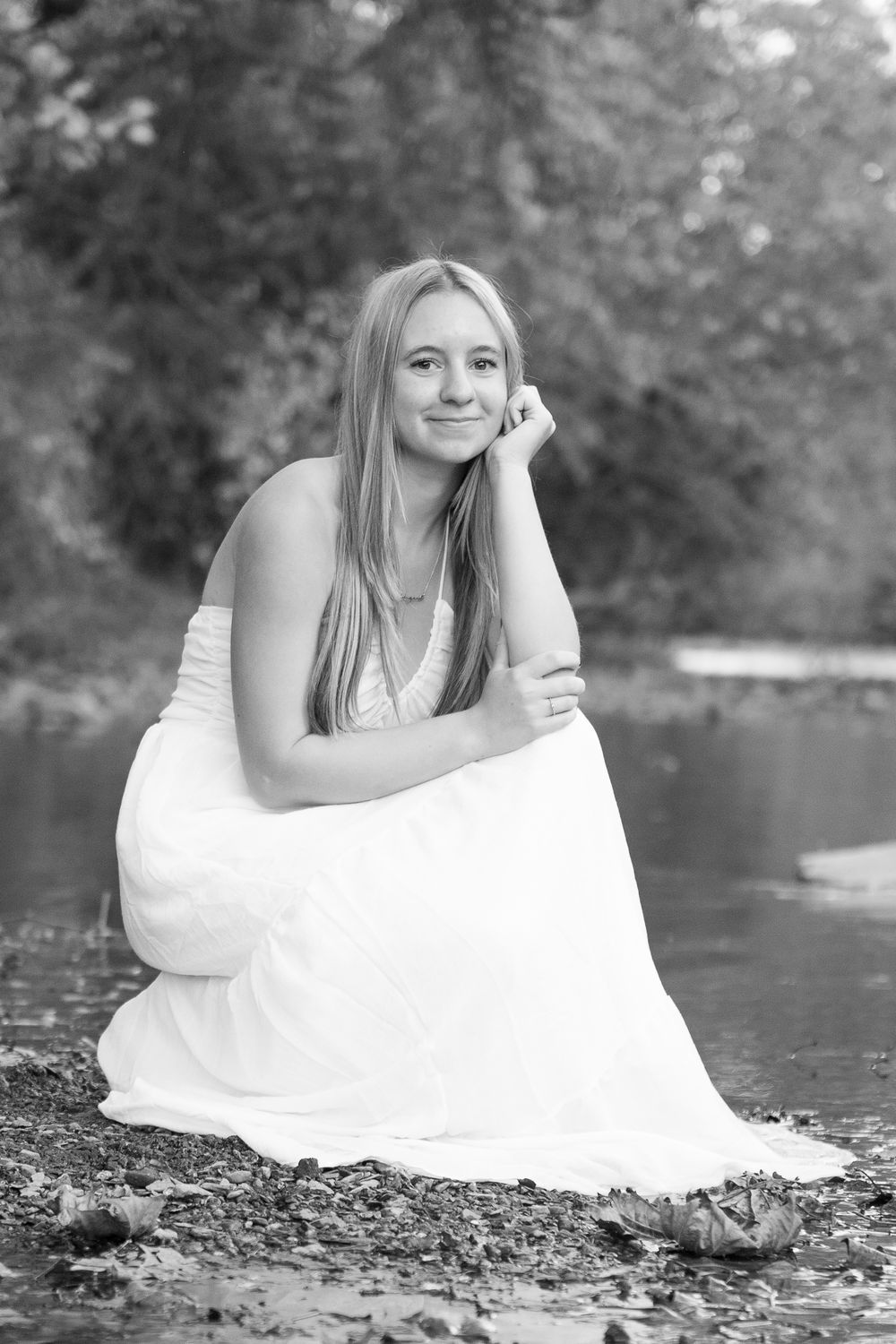 Black and white artistic photo series of a person in a white dress reclining on rocks by a river.