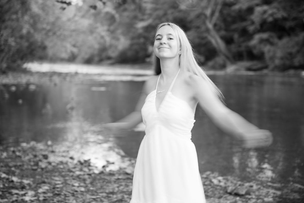 A series of black and white photos showing someone in a white dress posing by a lake in nature.