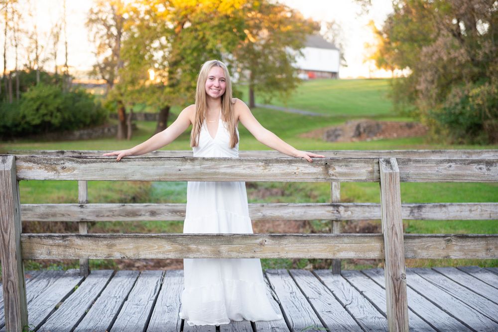 A bride in a white wedding dress poses on a rustic wooden deck surrounded by autumn foliage.