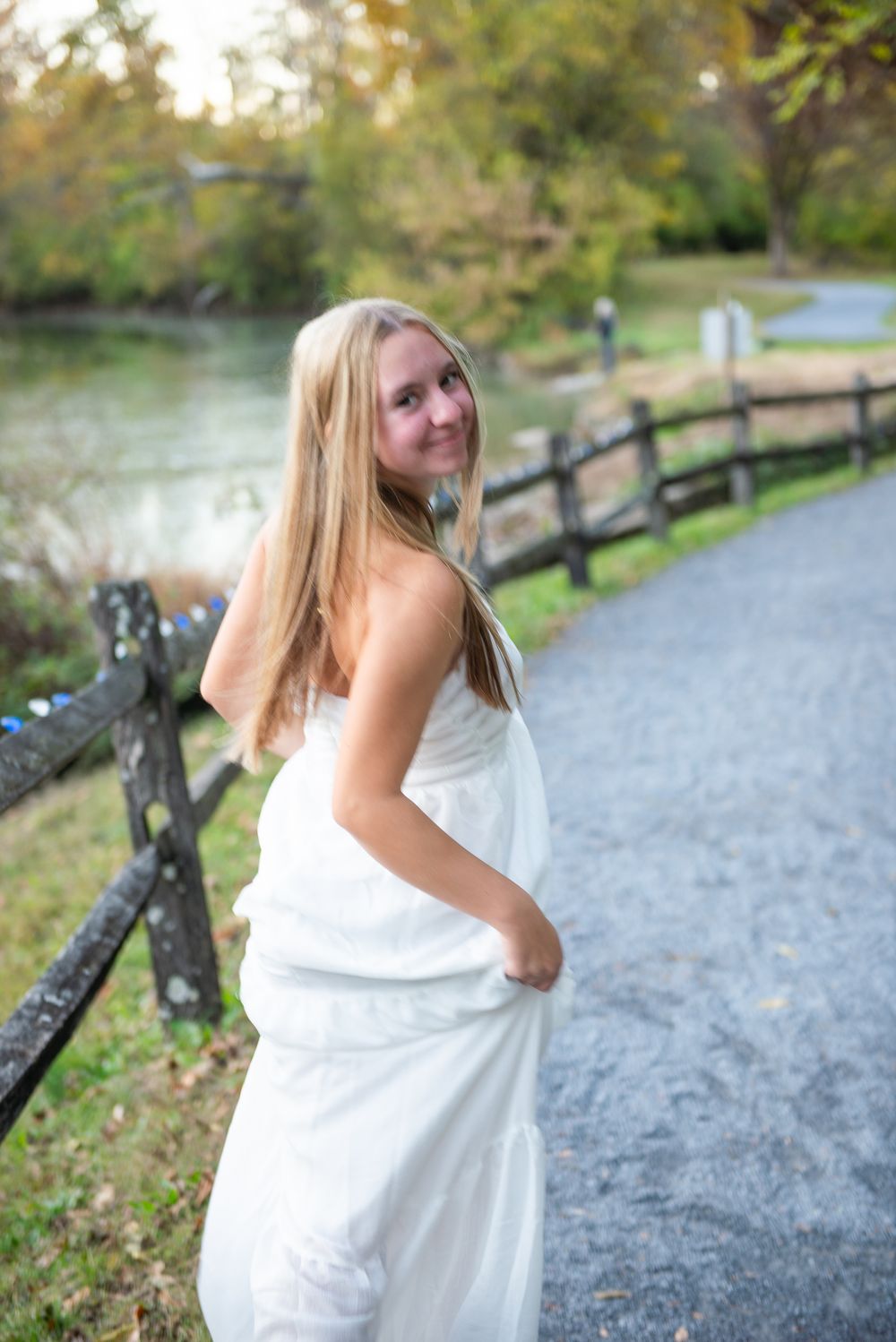 Outdoor portrait session along gravel path with rustic split rail fence and autumn foliage.