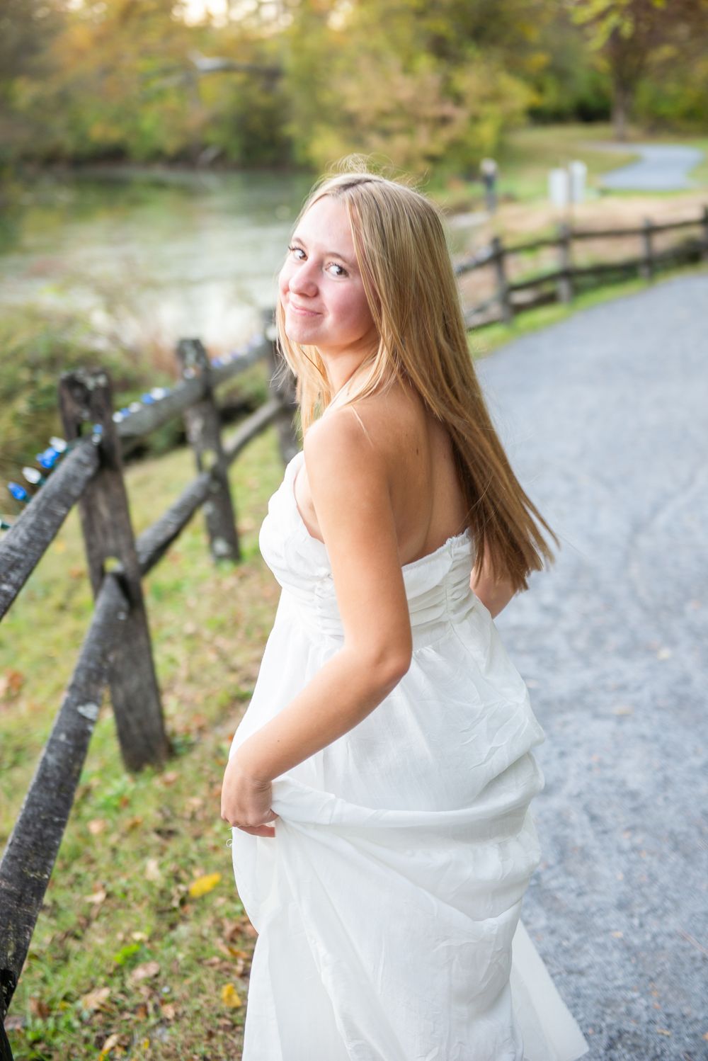 Candid moments captured along scenic park trail with white dress against natural fall backdrop.
