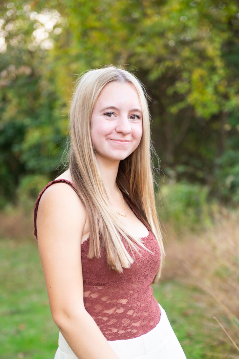 A person in a burgundy top poses outdoors against a blurred green natural background.