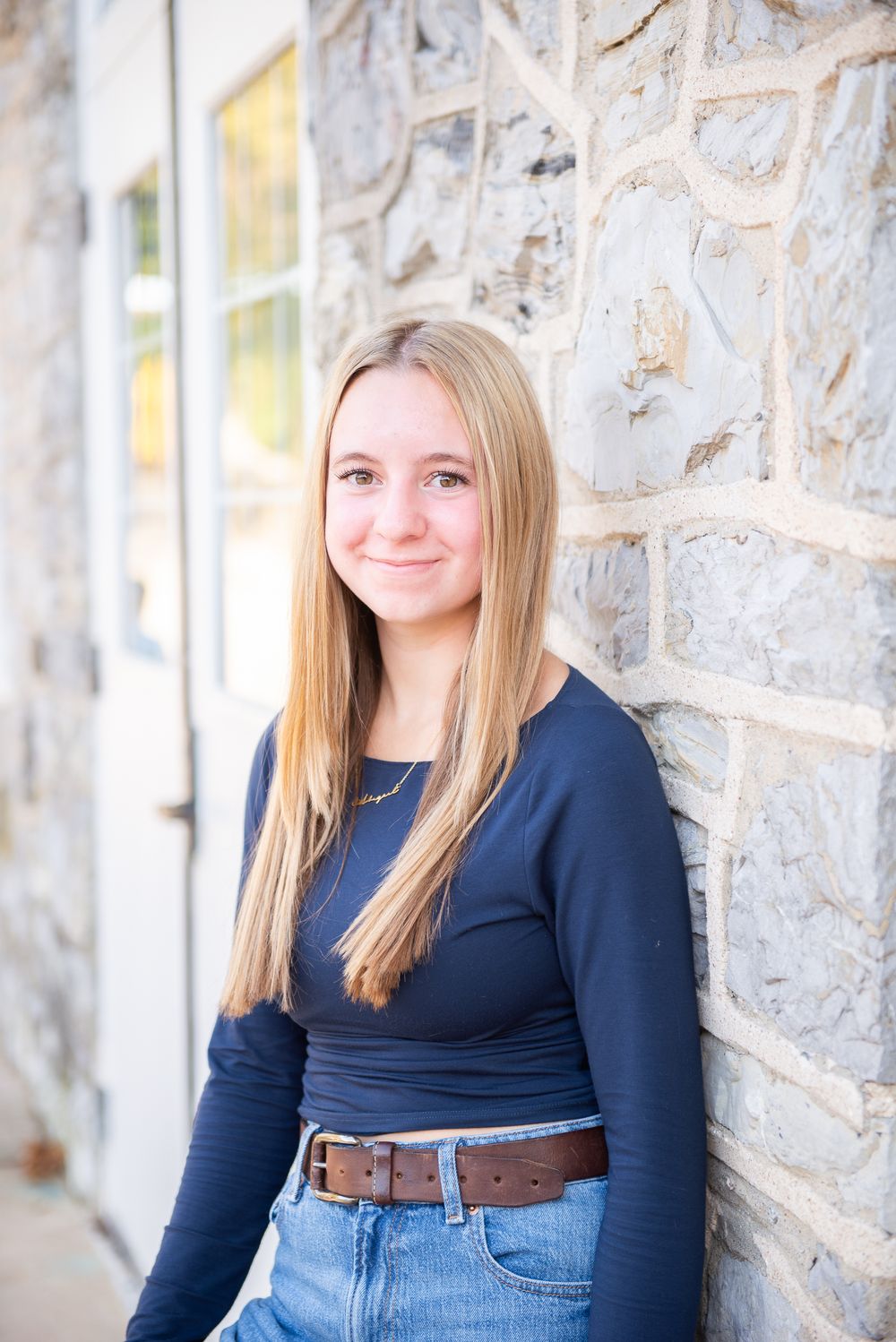 A series of outdoor portrait photos showing someone in a navy blue top and jeans against a stone wall background.