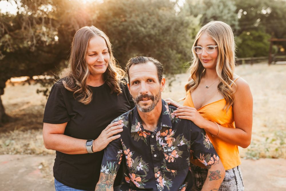 A group of people laugh and embrace during a golden hour photo session in a rustic outdoor setting.
