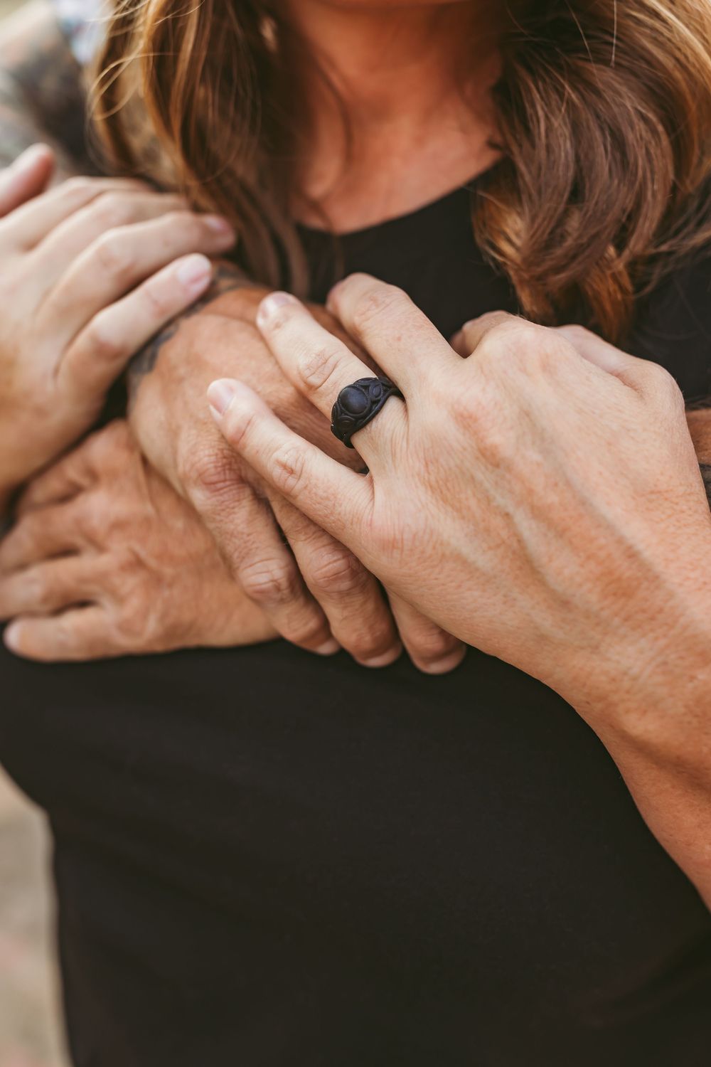 Close-up of hands wearing rings intertwined against a black background showing intimate connection and detail.