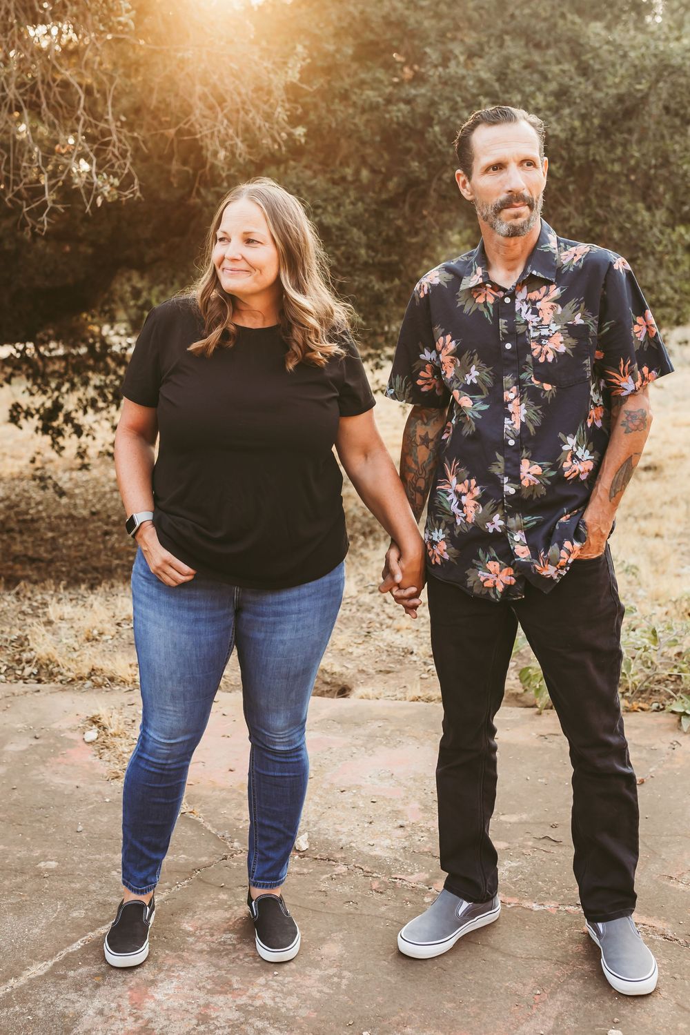 A couple stands together showing their shoes and casual outfits during an outdoor photo session.