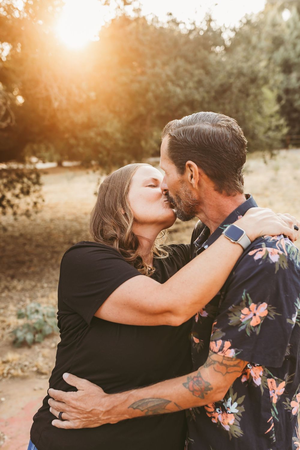 Romantic couple embraces and kisses during golden hour sunset in a desert landscape setting.