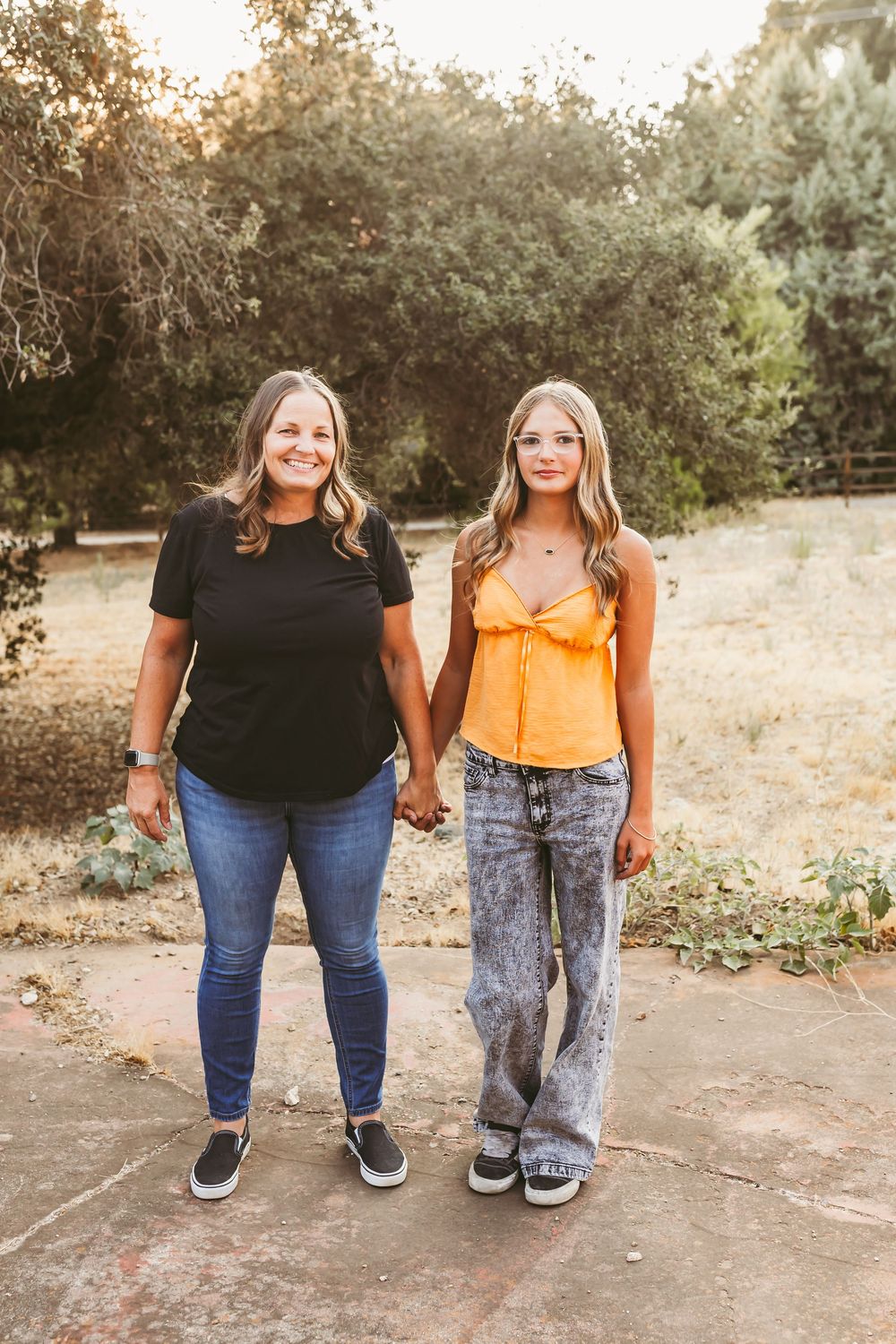 Two people standing together wearing casual outfits of jeans and t-shirts shown from waist down in an outdoor setting.