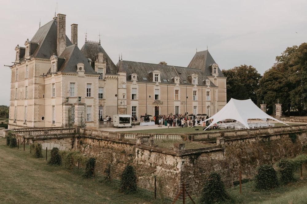 Panoramic view of a historic French castle with stone walls and turrets under overcast skies.