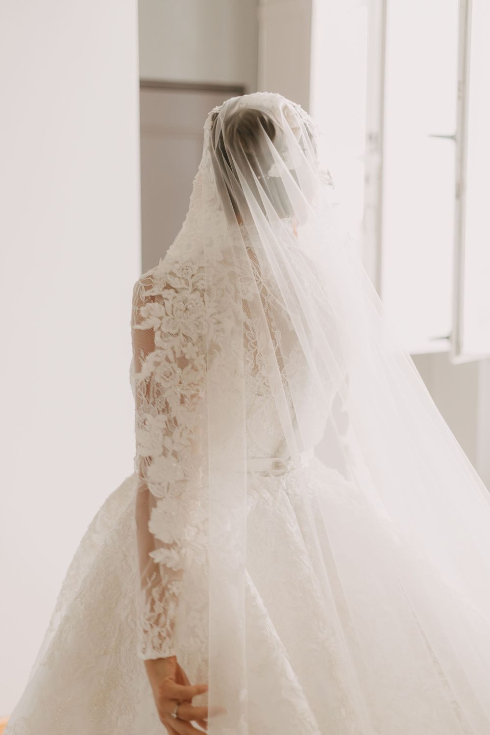 Delicate lace details and flowing veil of a classic white wedding gown in natural light.