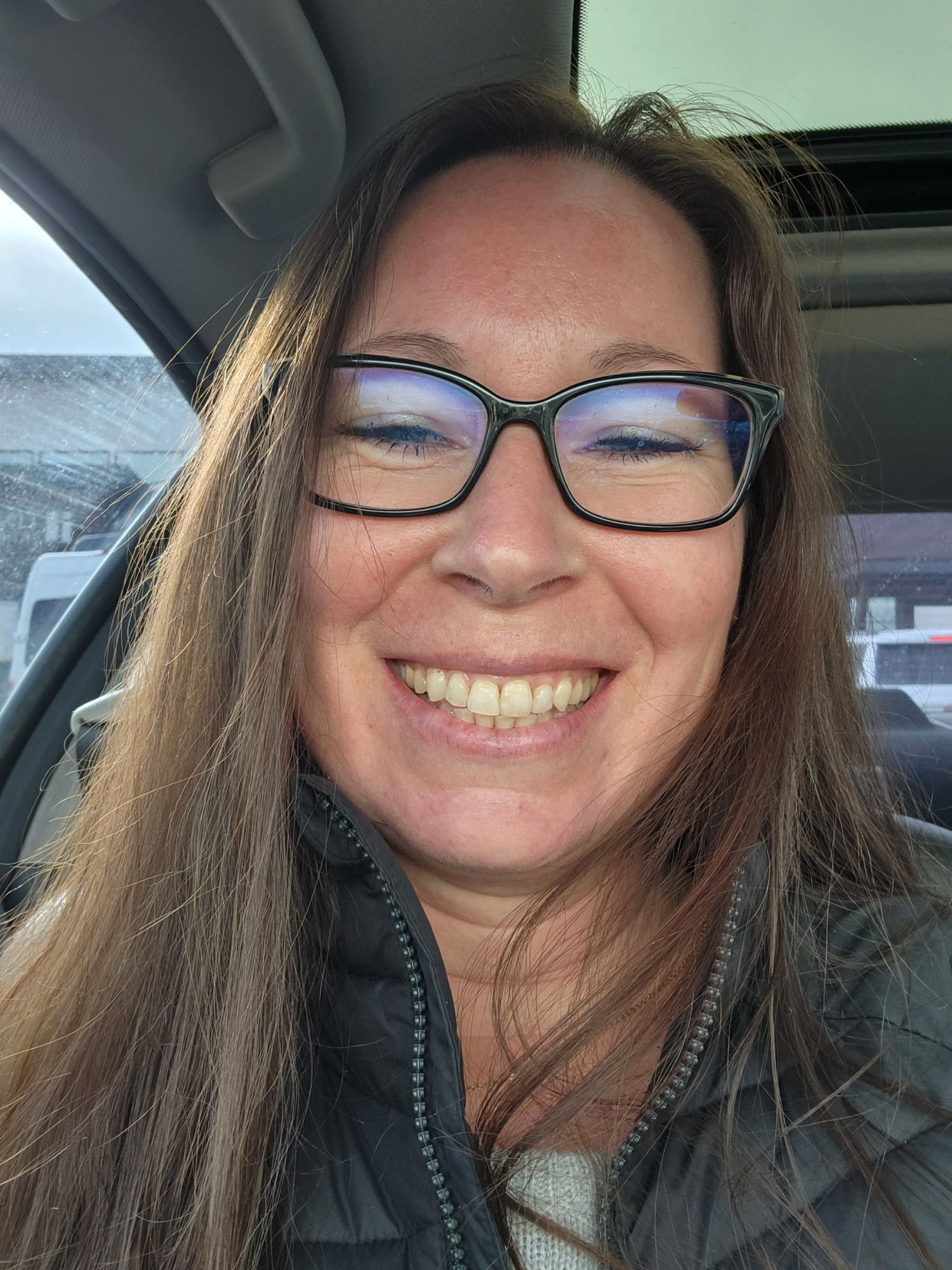 A person wearing glasses smiles warmly while sitting in a car, captured in a series of selfie photos.