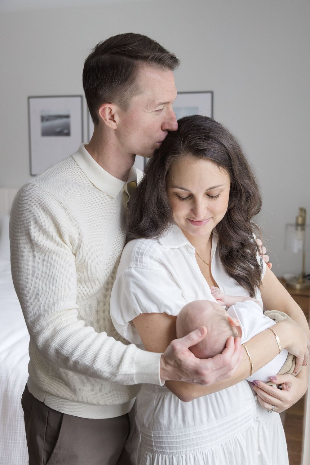 "Parents holding their newborn during in-home lifestyle session in Washington DC, father kissing mother's head."