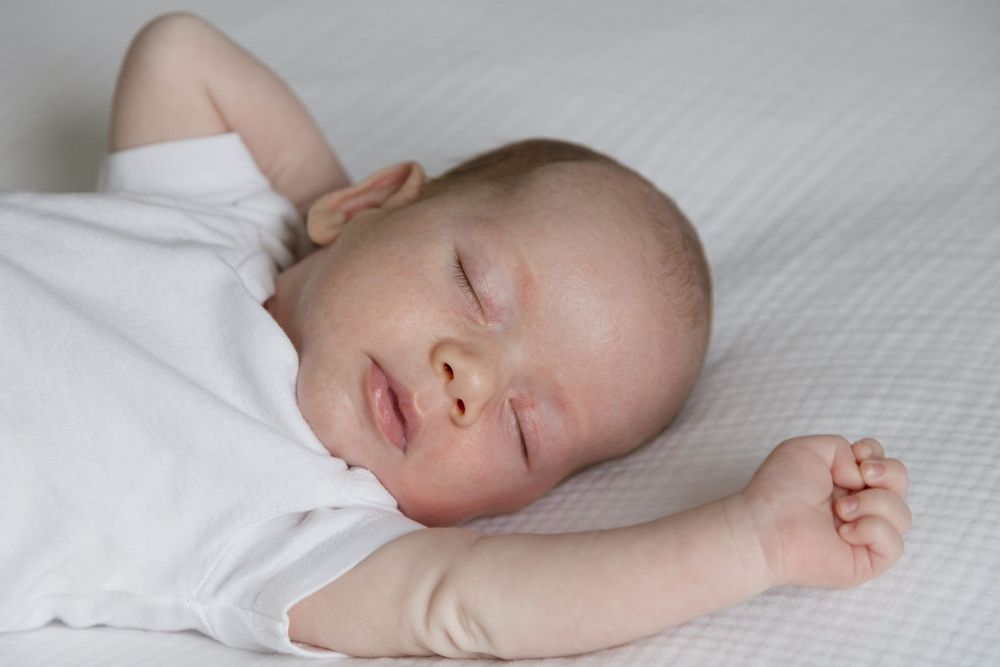 "Newborn baby stretching on parents' bed during in-home cozy lifestyle newborn session in Washington DC near Bethesda and Chevy Chase."