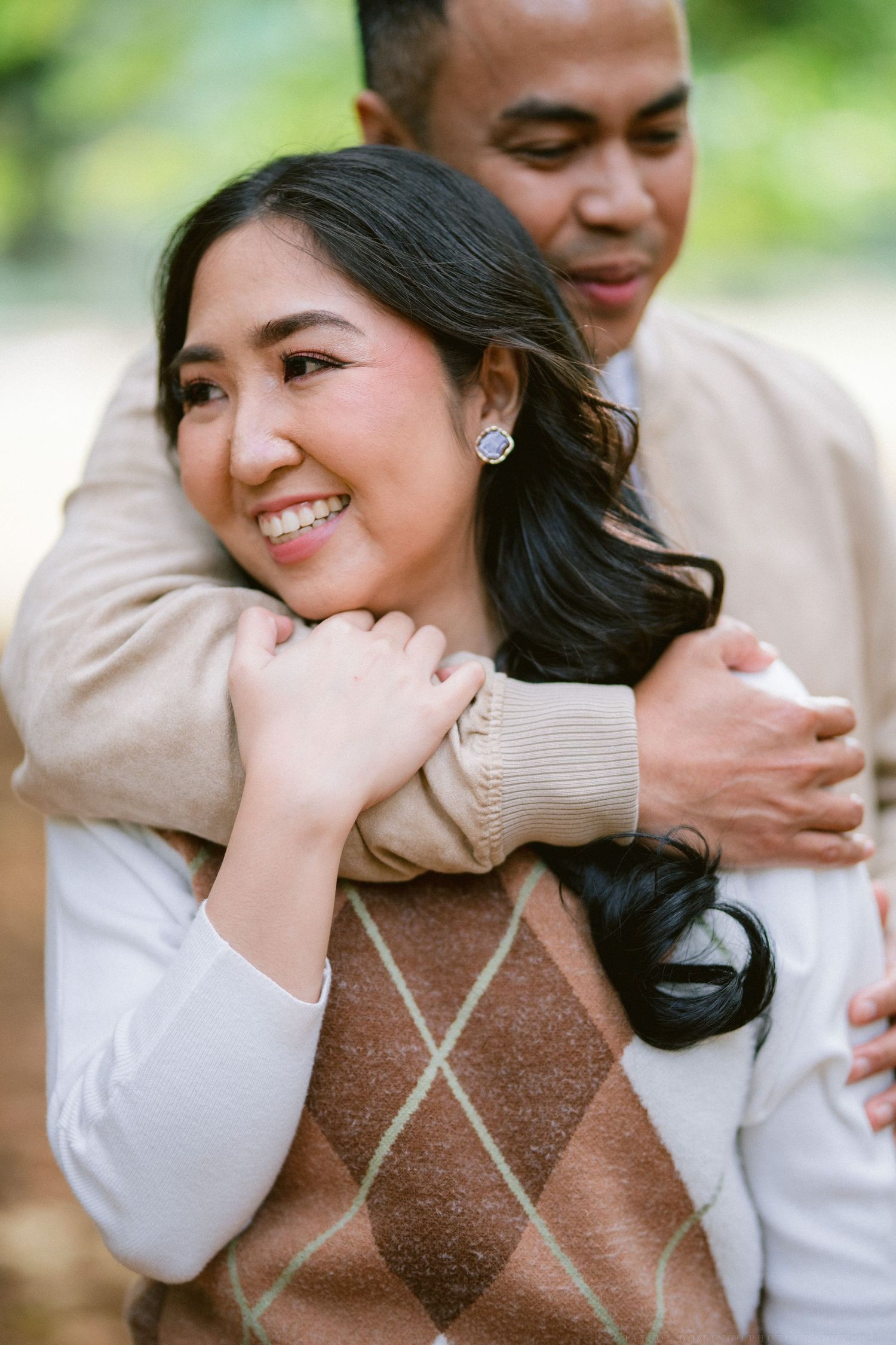 A couple embraces while wearing coordinating beige and white sweaters during an outdoor photoshoot.