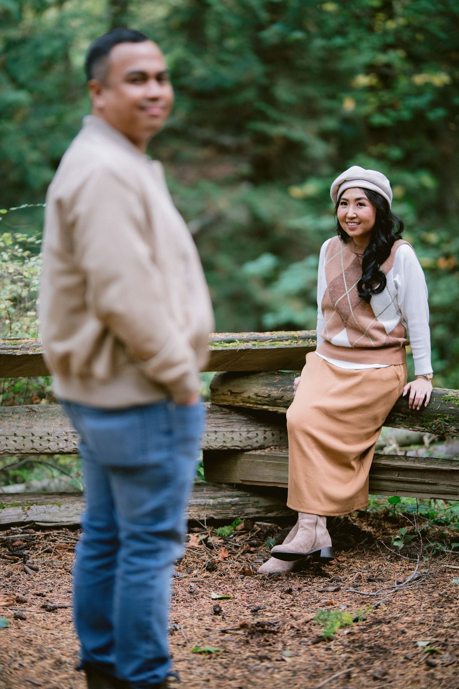 Couple sitting on rustic wooden fence in a forest setting wearing casual fall attire.