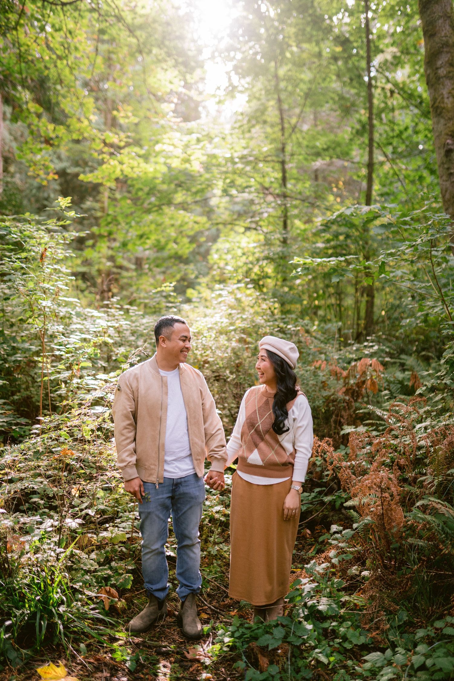 A couple shares a romantic moment while walking through a lush forest path in autumn.