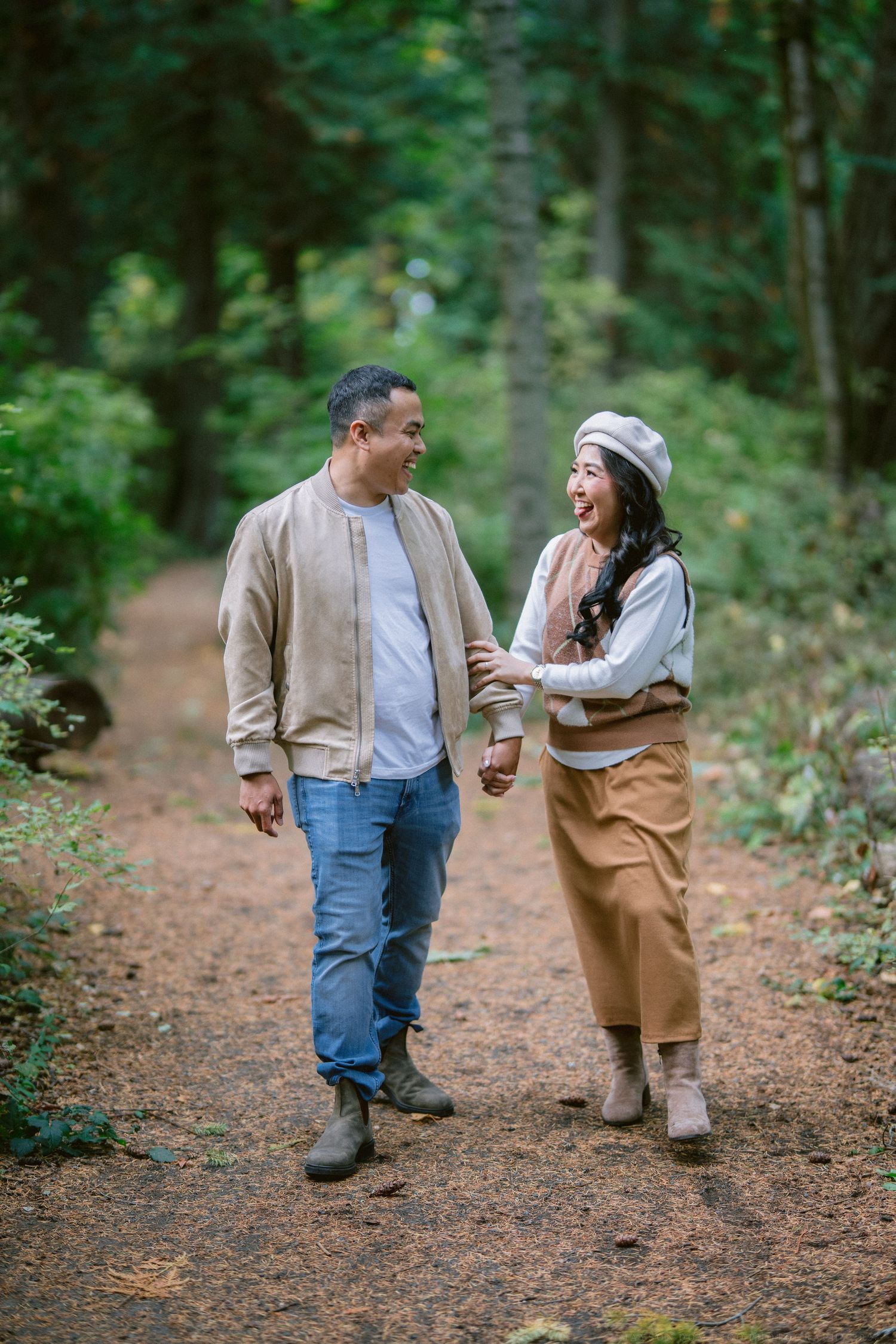 A couple walks together on a forest path while engaged in playful conversation and laughter.