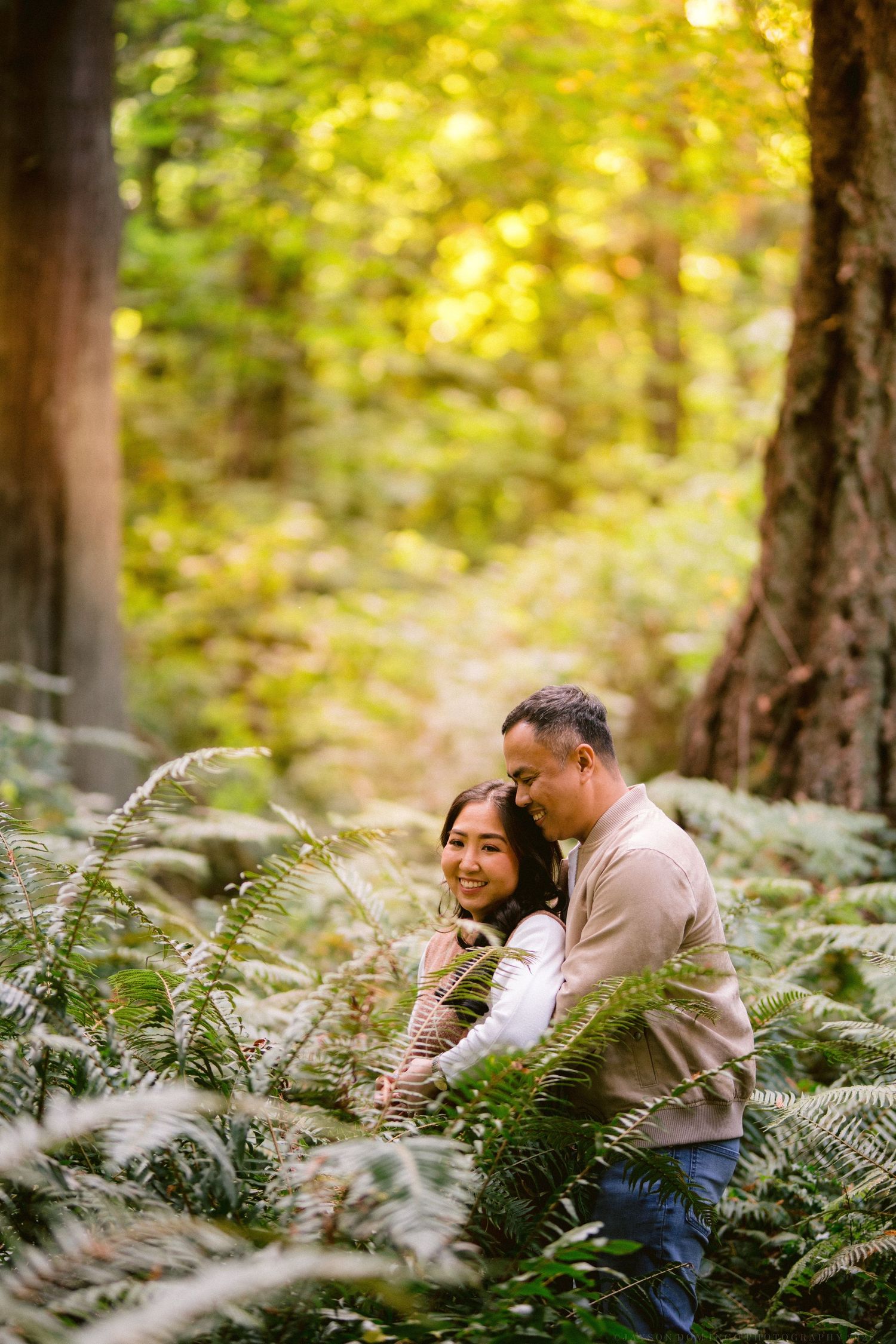 Couple nestled among ferns in a sunlit forest setting.