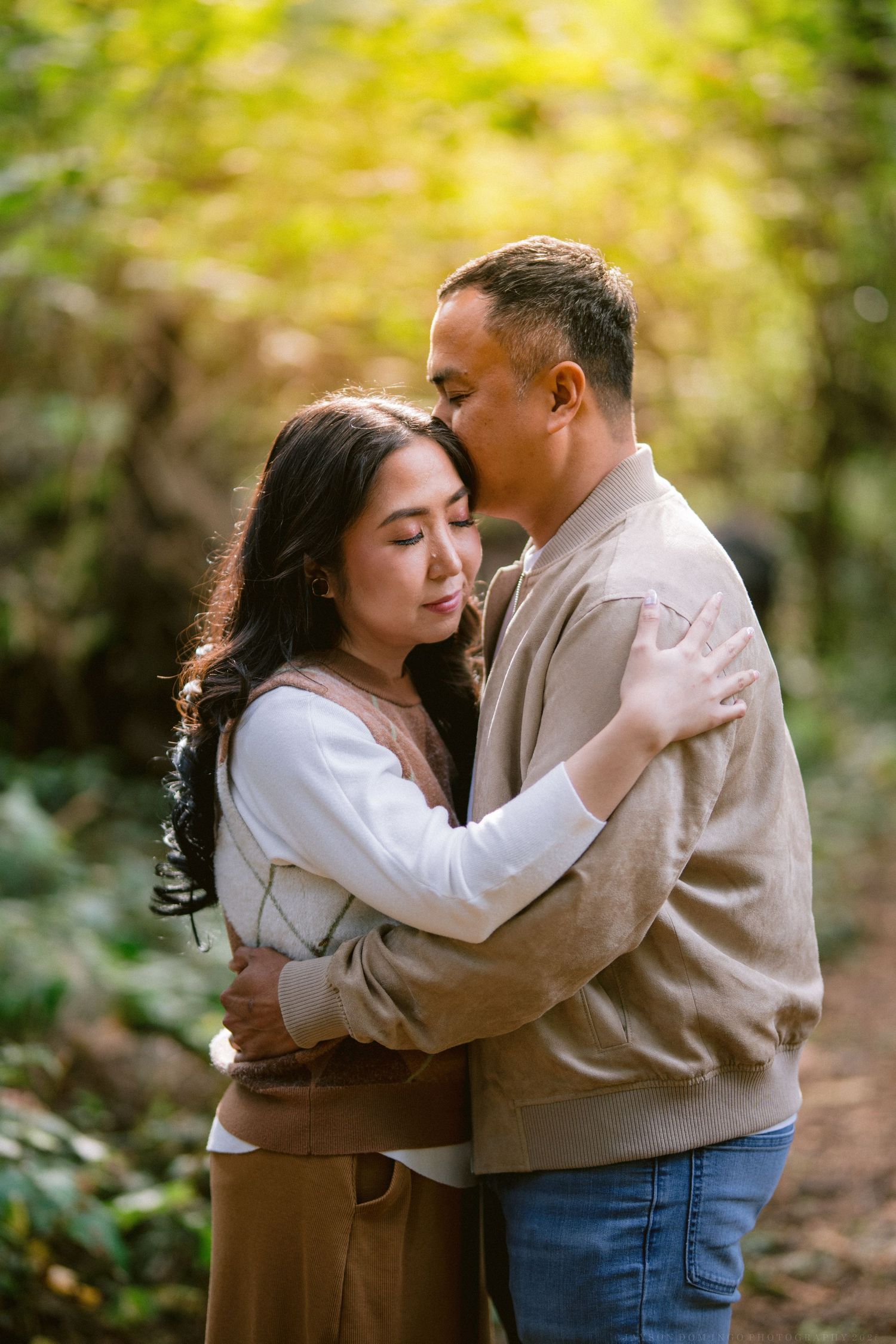 A romantic couple embraces in a natural outdoor setting with soft yellow foliage in the background.