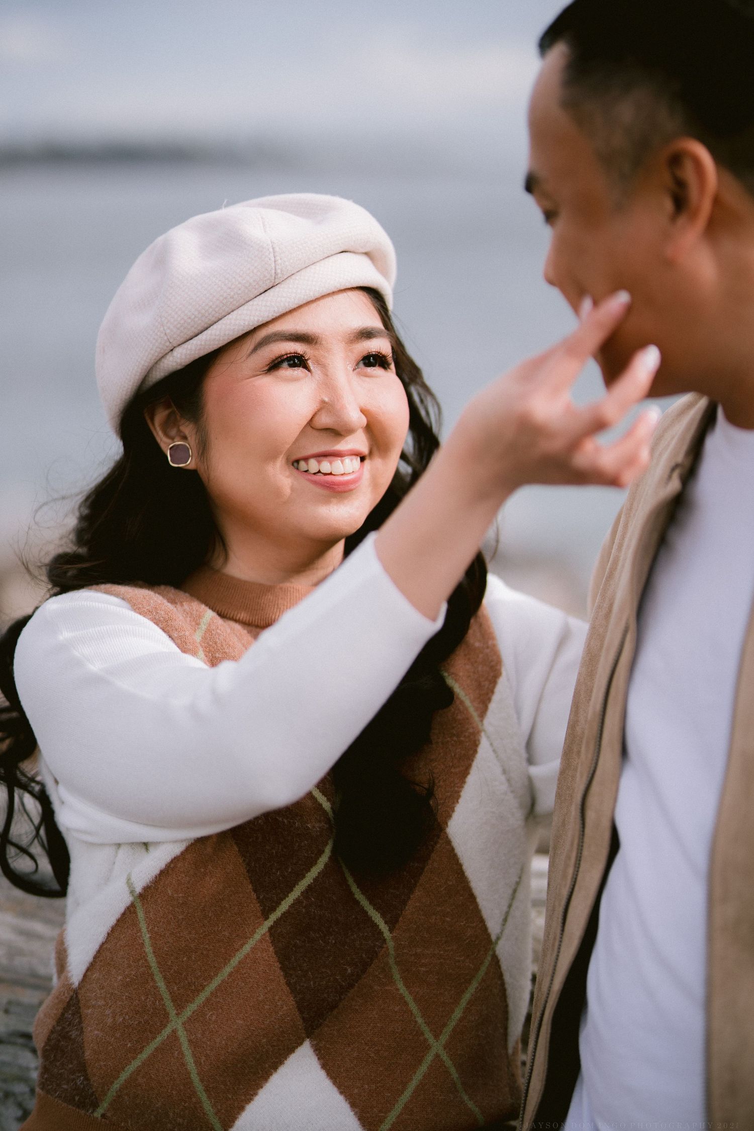 Intimate couple portrait session with warm knit sweaters and a cozy beanie against cloudy skies.