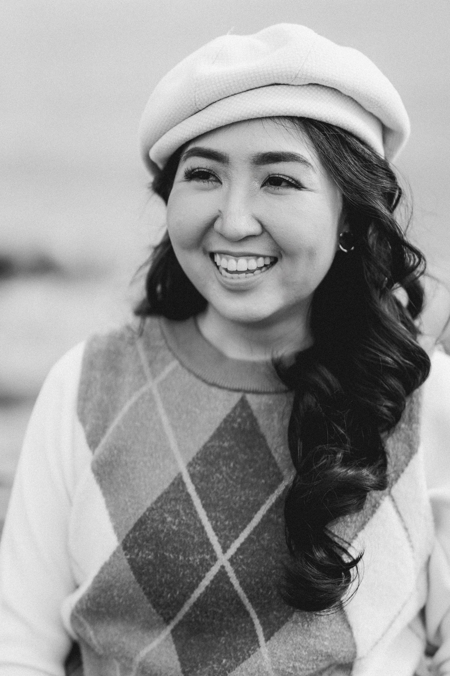Person wearing white beret and argyle sweater vest smiling warmly.