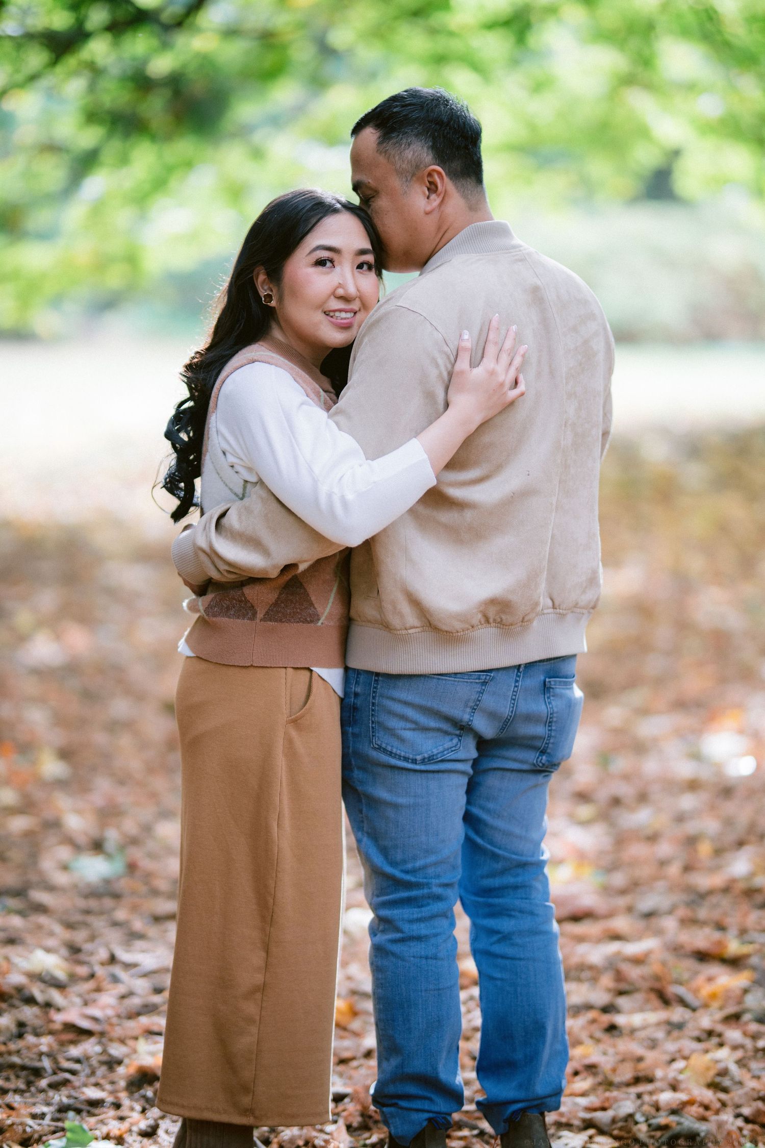 Couple in coordinated beige outfits embracing on autumn leaves.