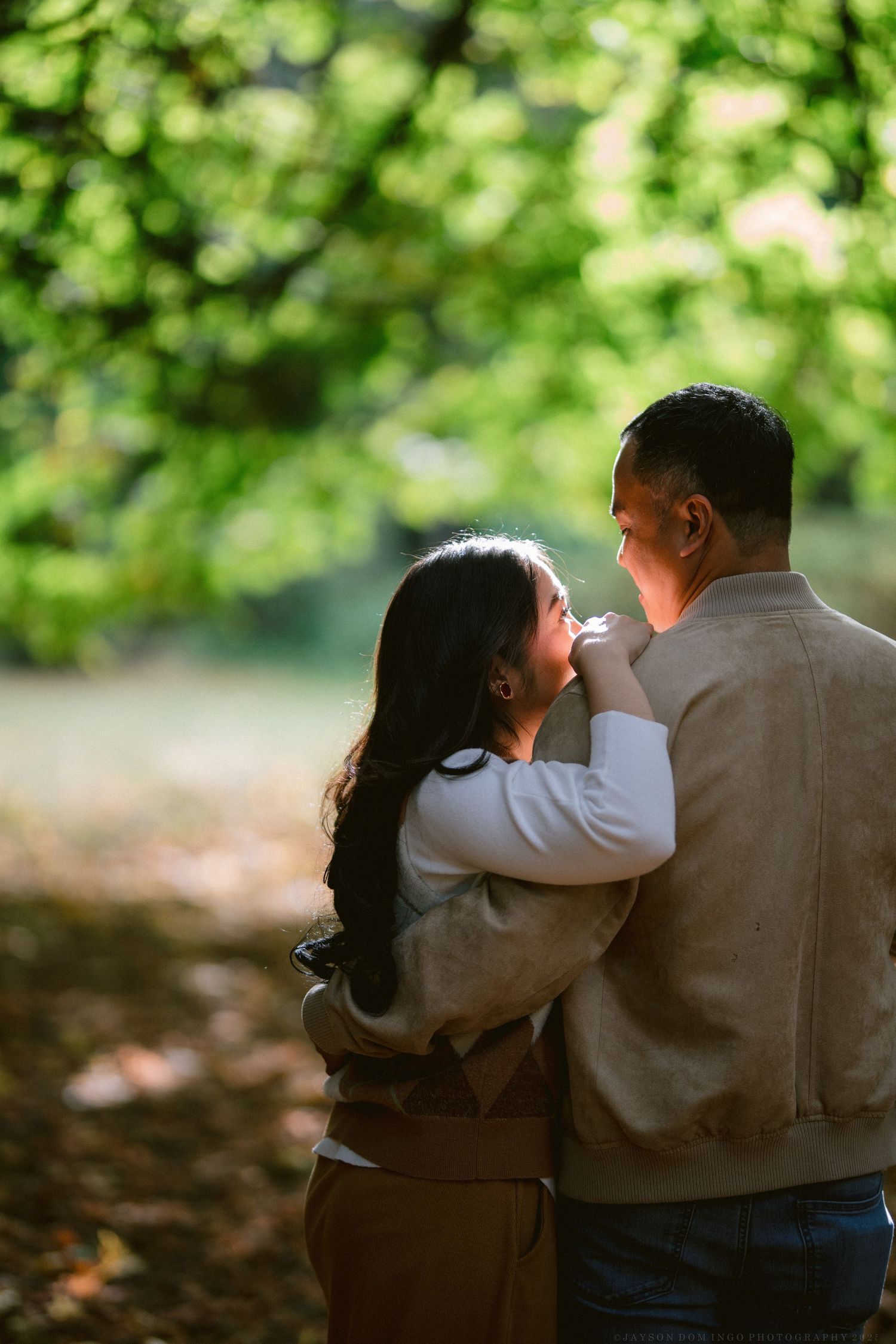A romantic couple sits close together on a bench in a lush green garden setting.