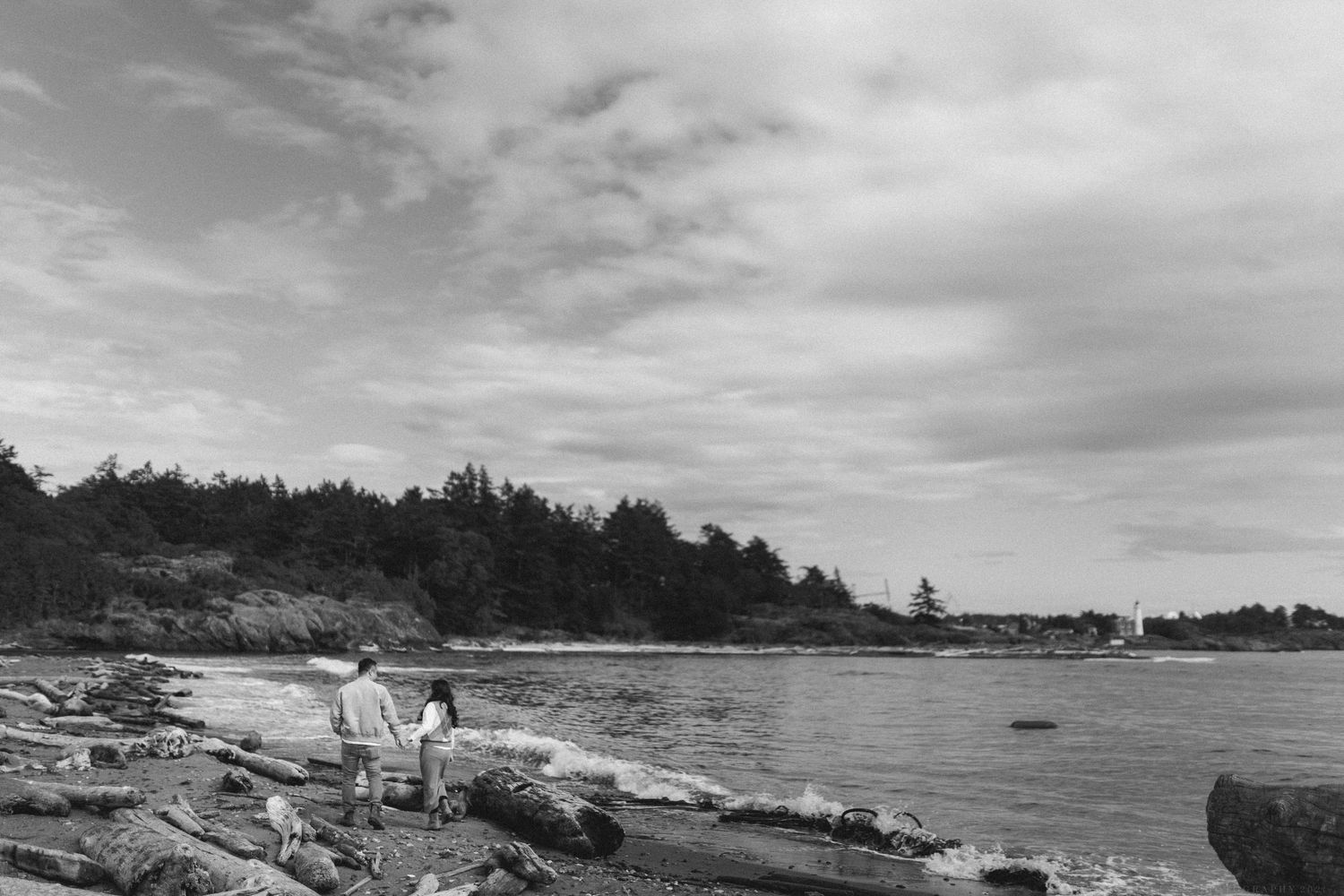A panoramic black and white coastal landscape showing a rocky shoreline and cloudy sky over a calm ocean bay.